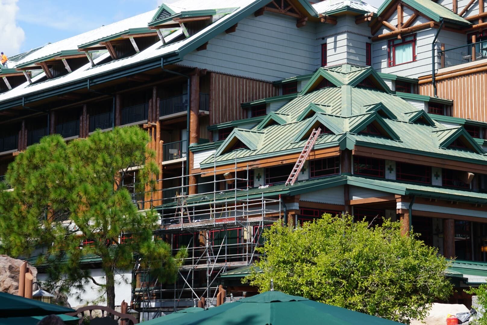 A building with green roofs and scaffolding on one side, surrounded by trees and partially sheltered by green awnings.