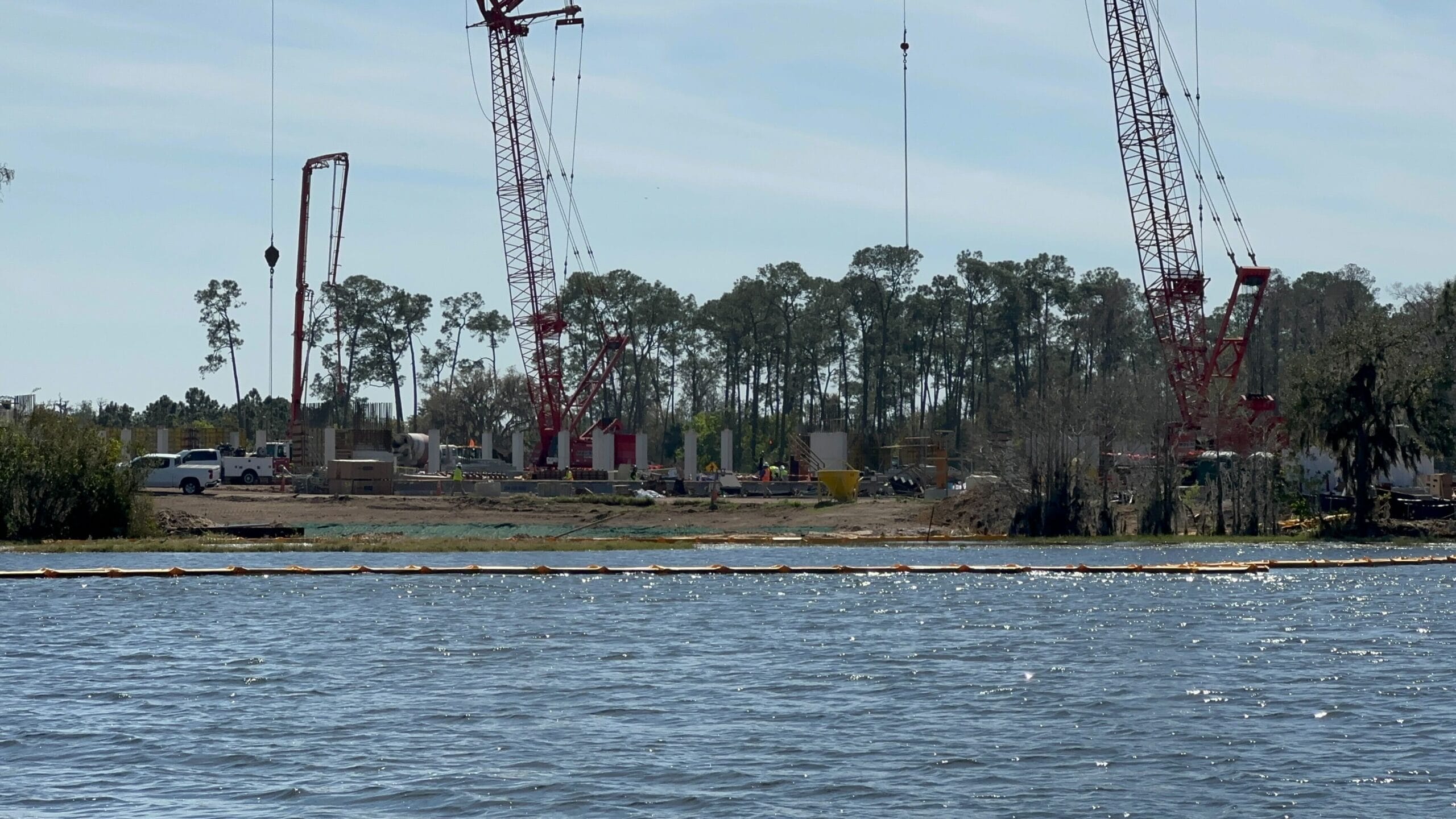 The construction site by a river, nestled near a forested area, buzzes with cranes and equipment as part of the latest construction update.