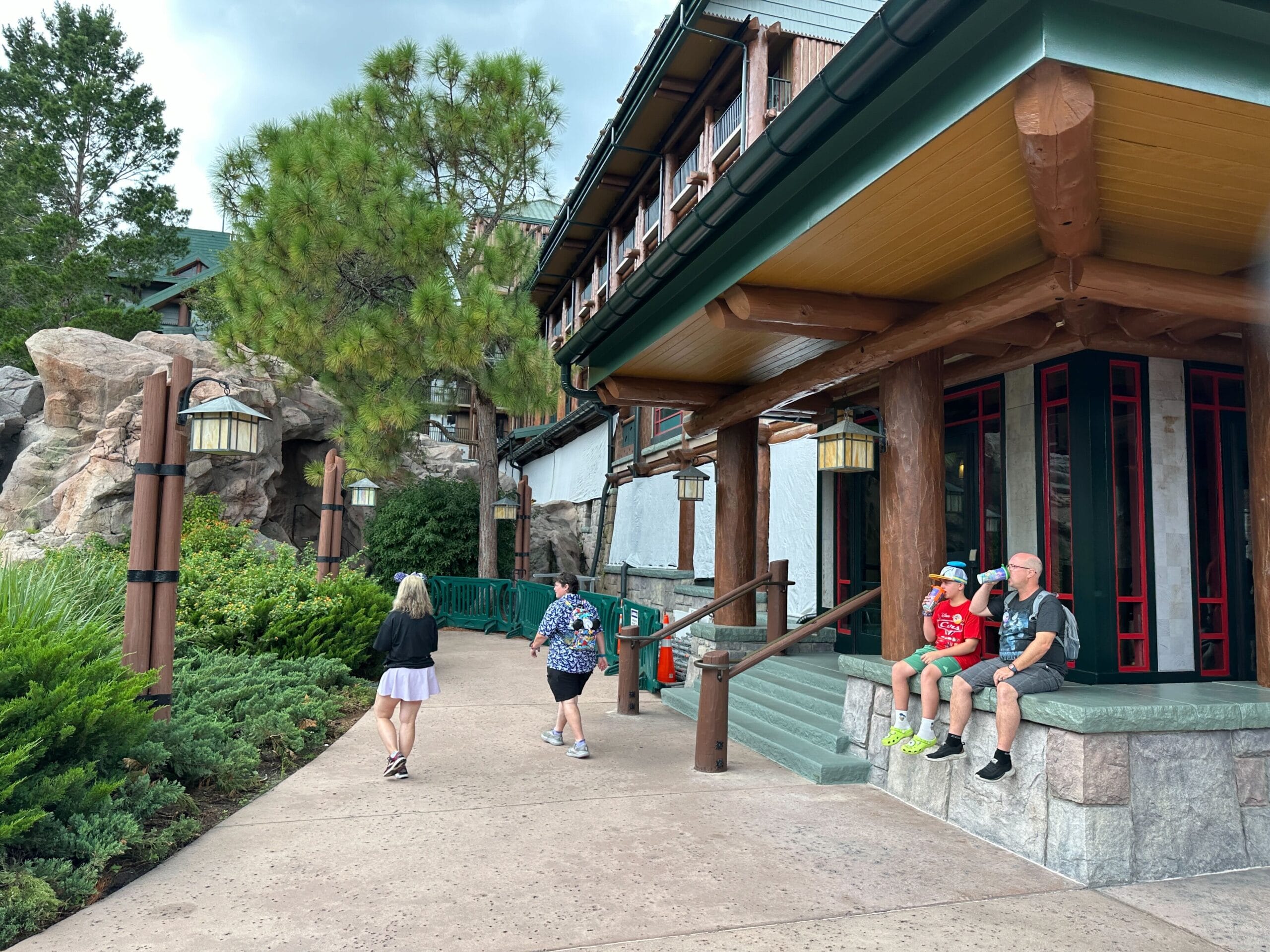 A family sits outside Wilderness Lodge while others walk by on a cloudy day.
