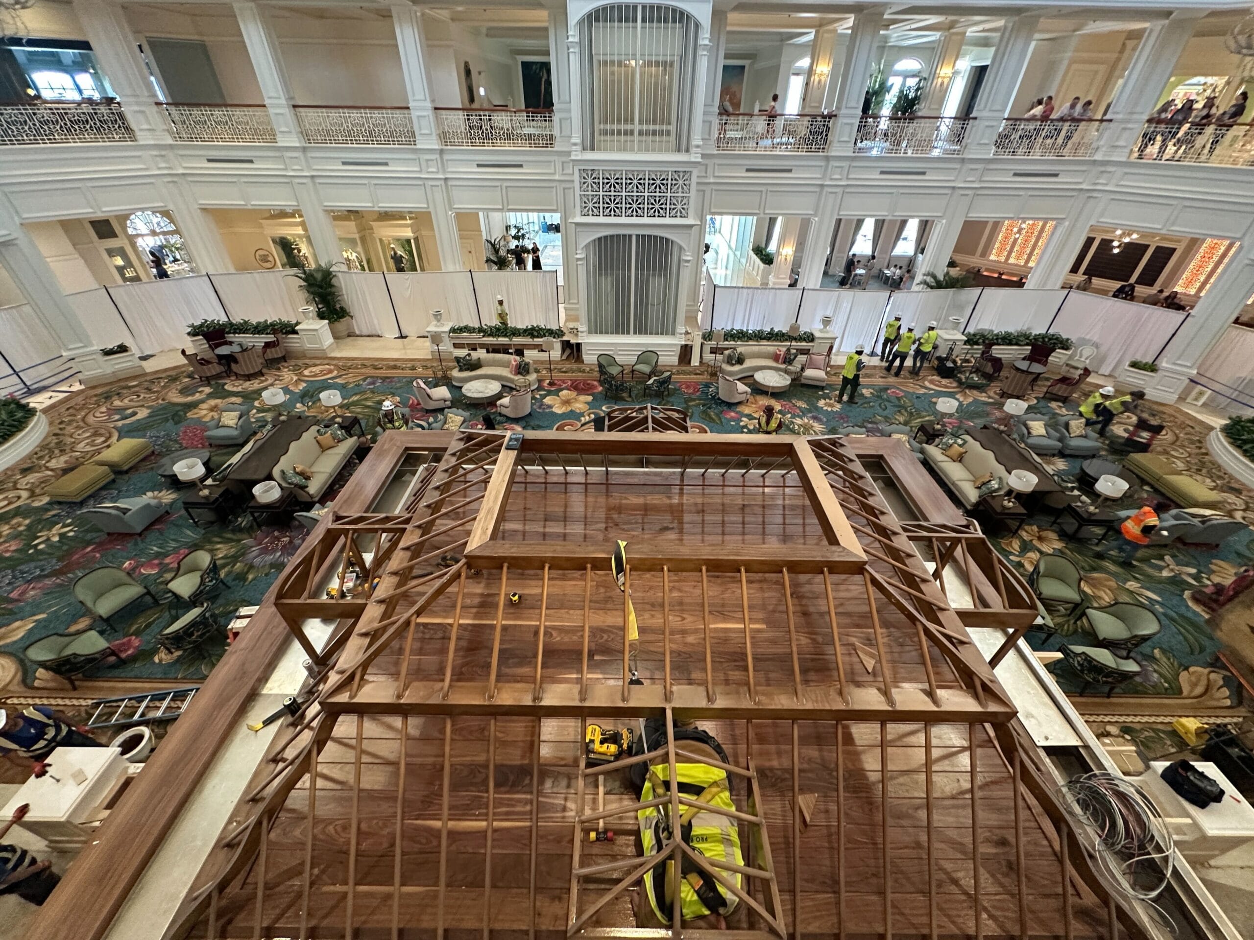 Workers build a wooden structure in Disney's Grand Floridian lobby, elegant seating and ornate carpet evoke classic Disney resort charm.