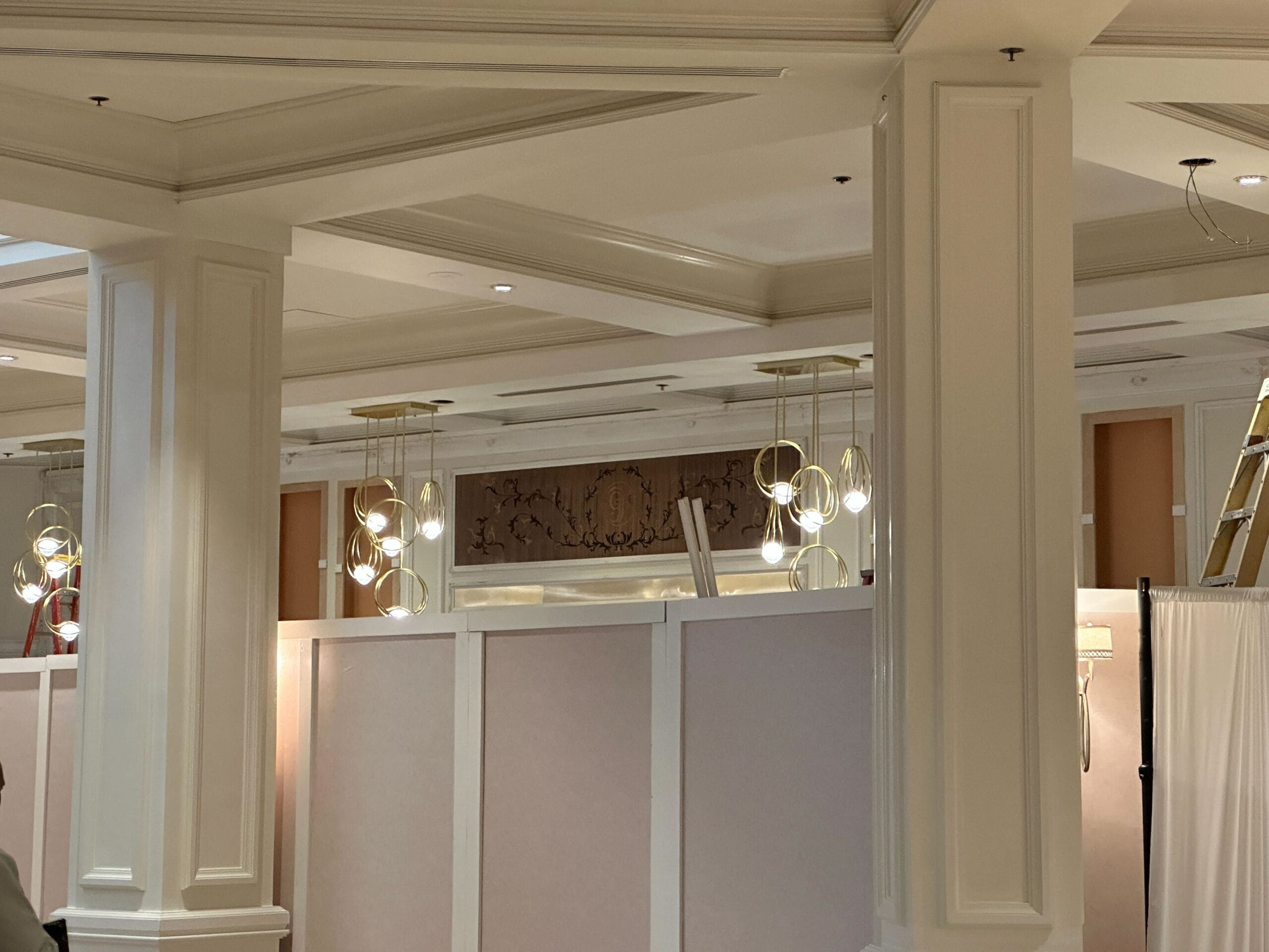 Modern light fixtures and a decorative wall are visible above temporary beige construction barriers and white columns indoors.