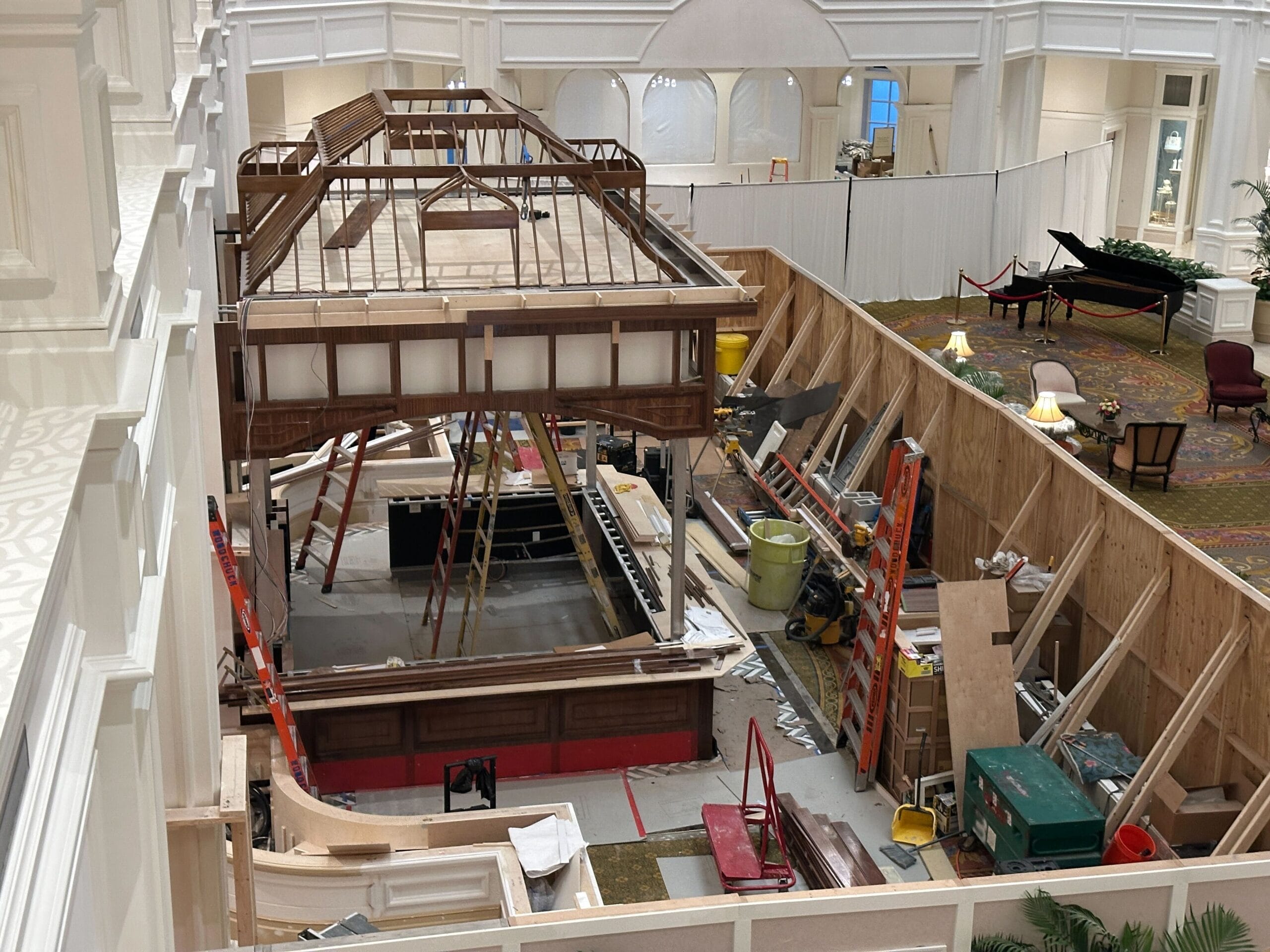 A large indoor construction site with wood framing, ladders, tools, and barriers in a spacious, elegant room.