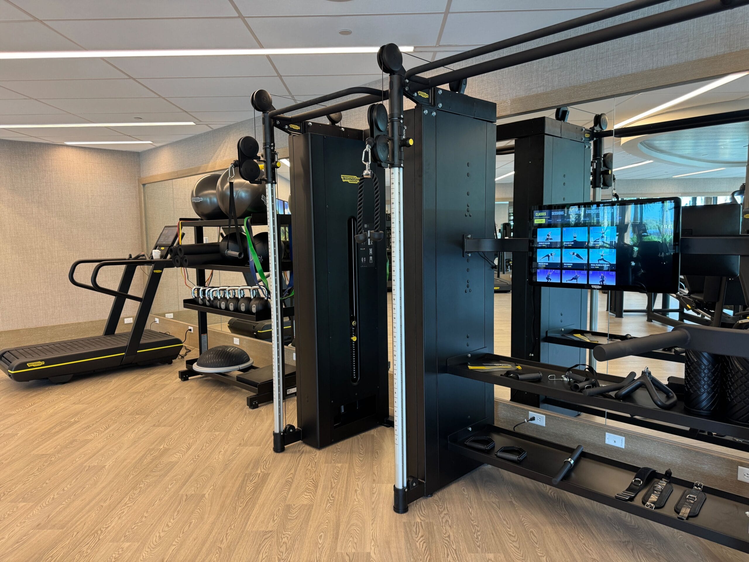A modern gym with treadmills, weights, and a multi-functional exercise machine, set on a wooden floor with mirrored walls.