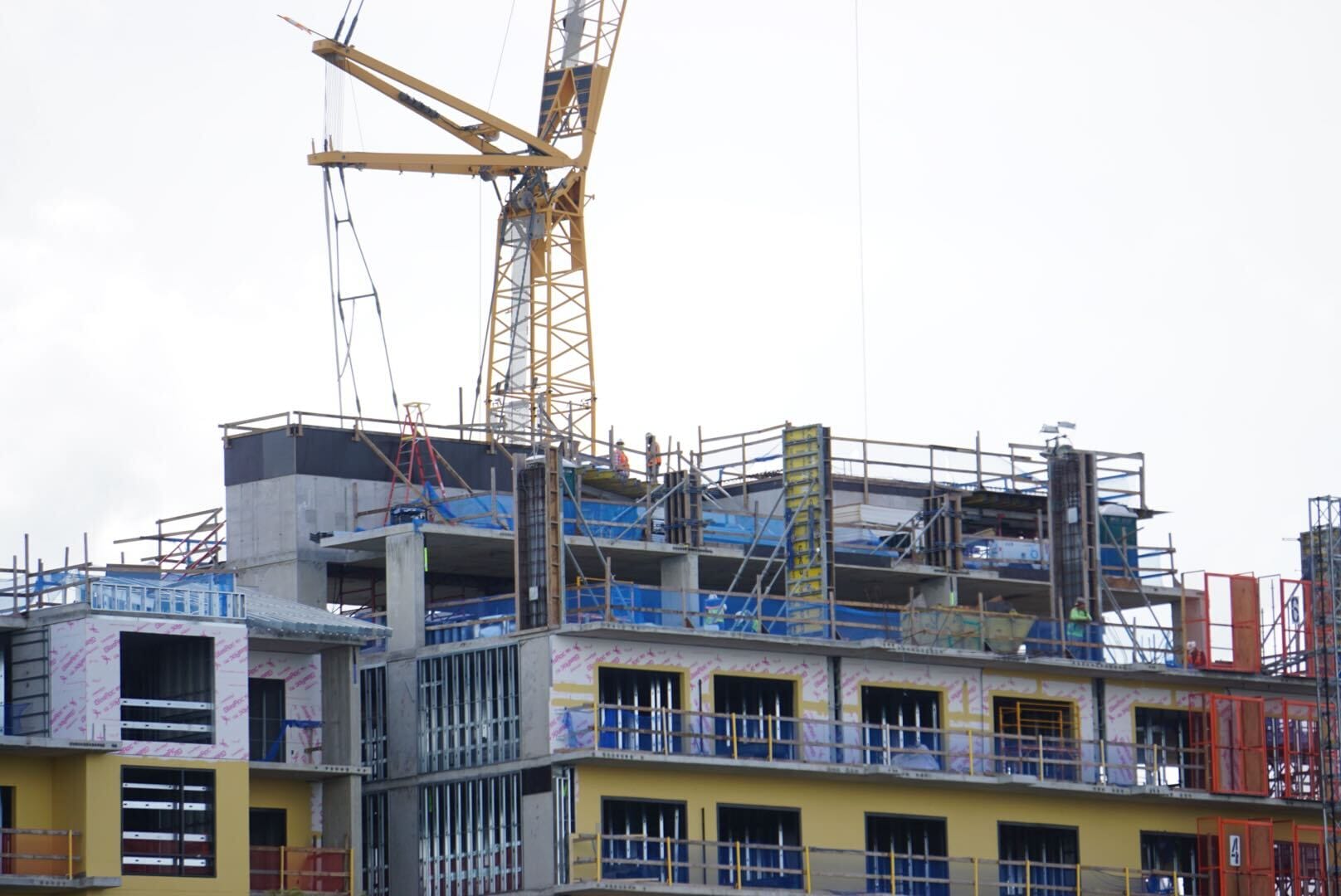 A crane and scaffolding surround a multi-story building under construction with workers on the upper floors.