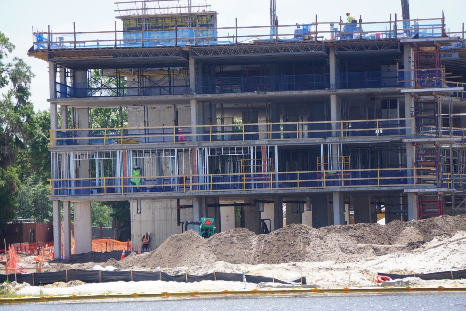 A multi-story building is under construction, with scaffolding and workers visible. Piles of dirt and construction equipment are in the foreground.