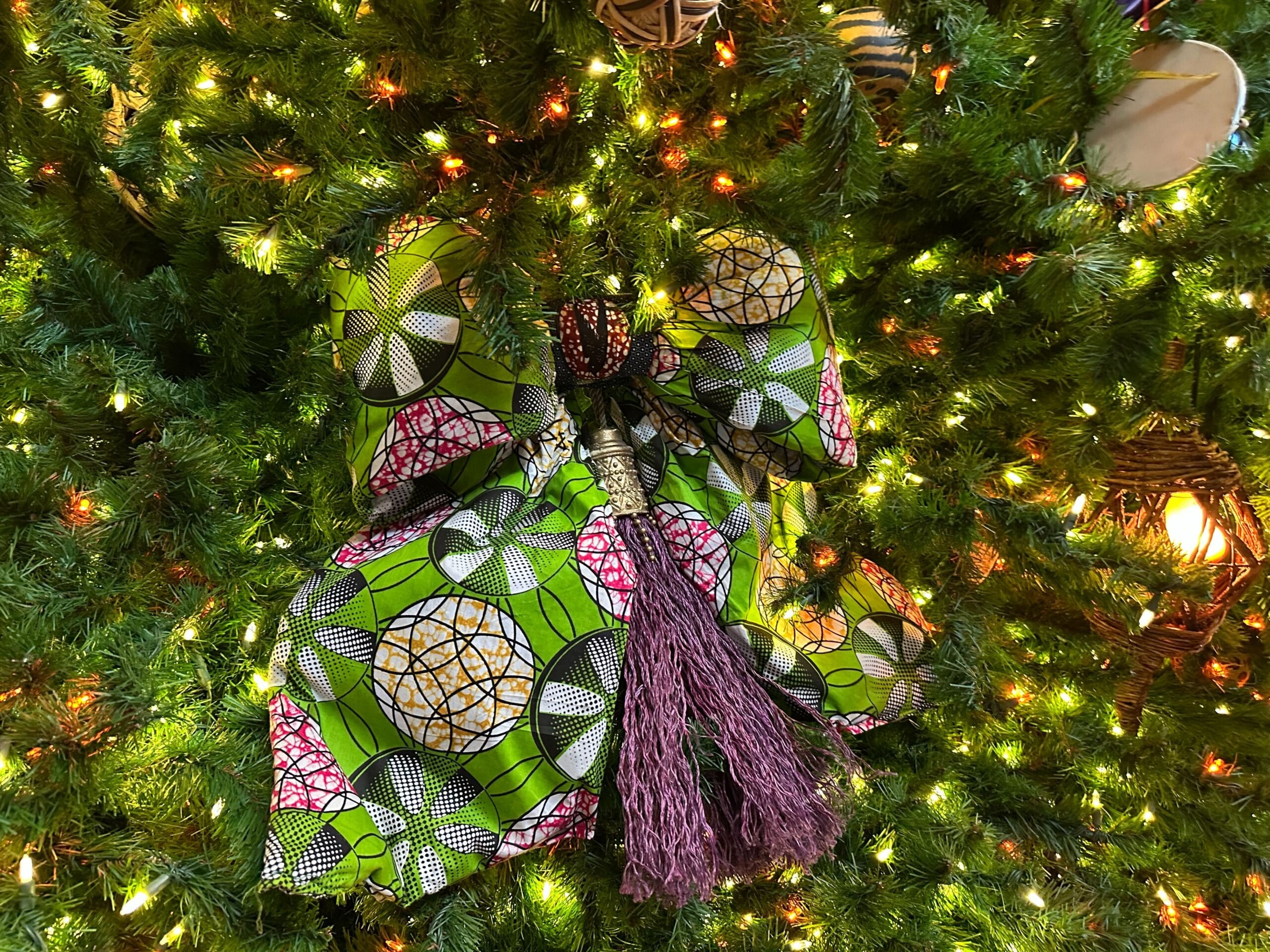 A colorful bow with vibrant patterns and a pink tassel is displayed on a decorated Christmas tree with bright lights.
