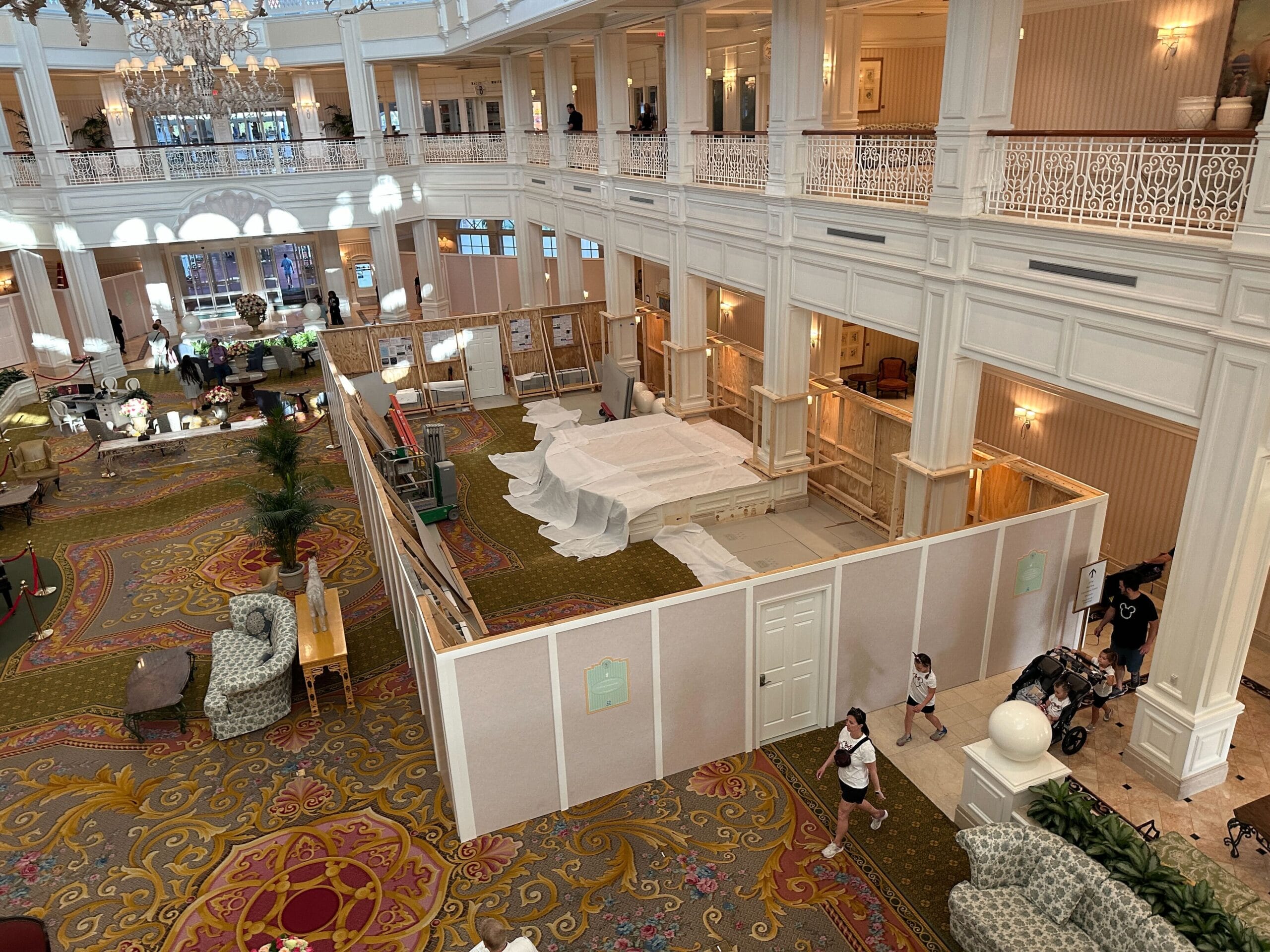 A large hotel lobby with ornate decor, guests walking by a fenced-off h2o glow after hours food construction area.