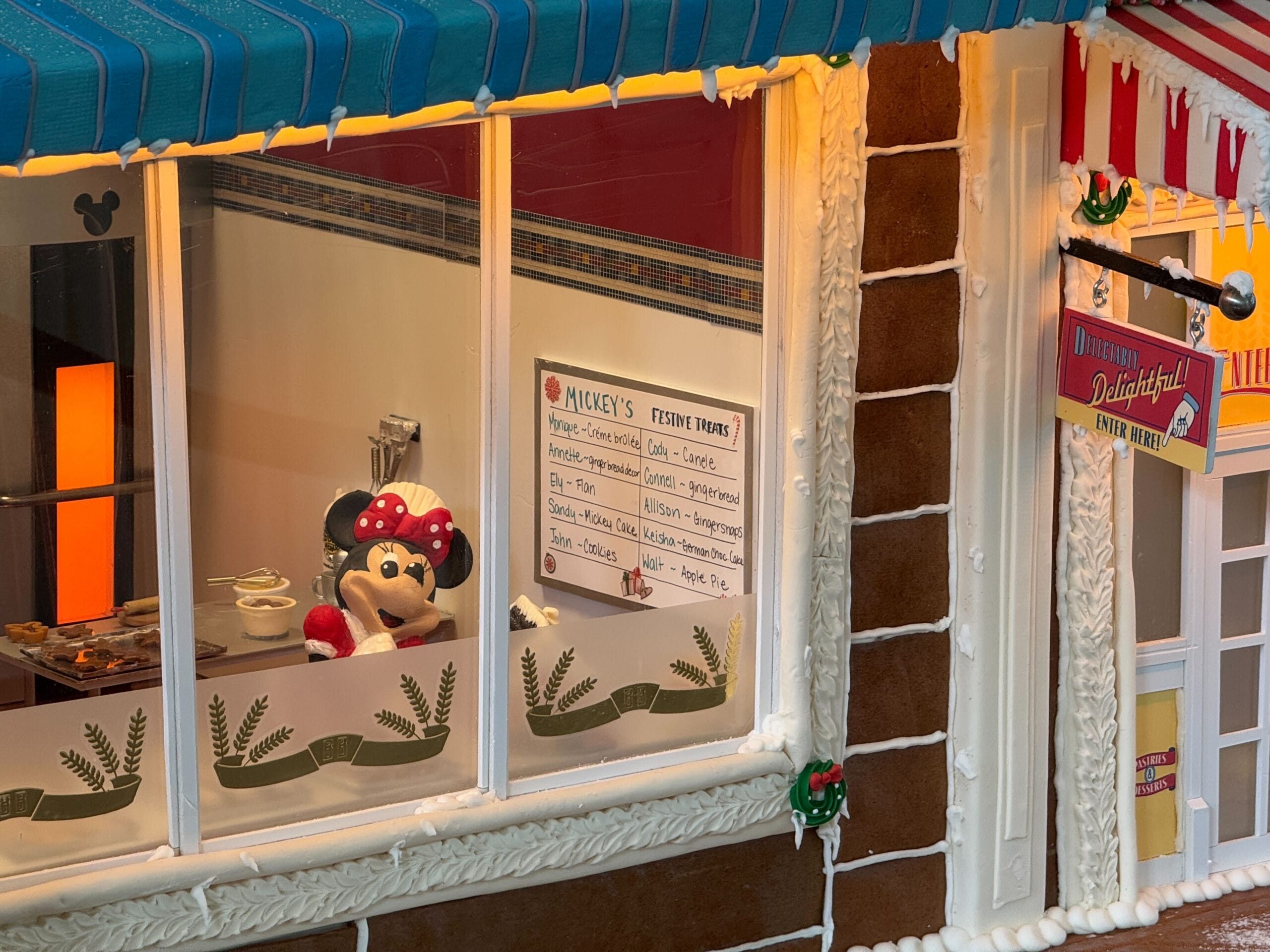 A miniature scene with a mouse character in a bakery setting, featuring a menu board with festive treats, gingerbread walls, and holiday decorations.