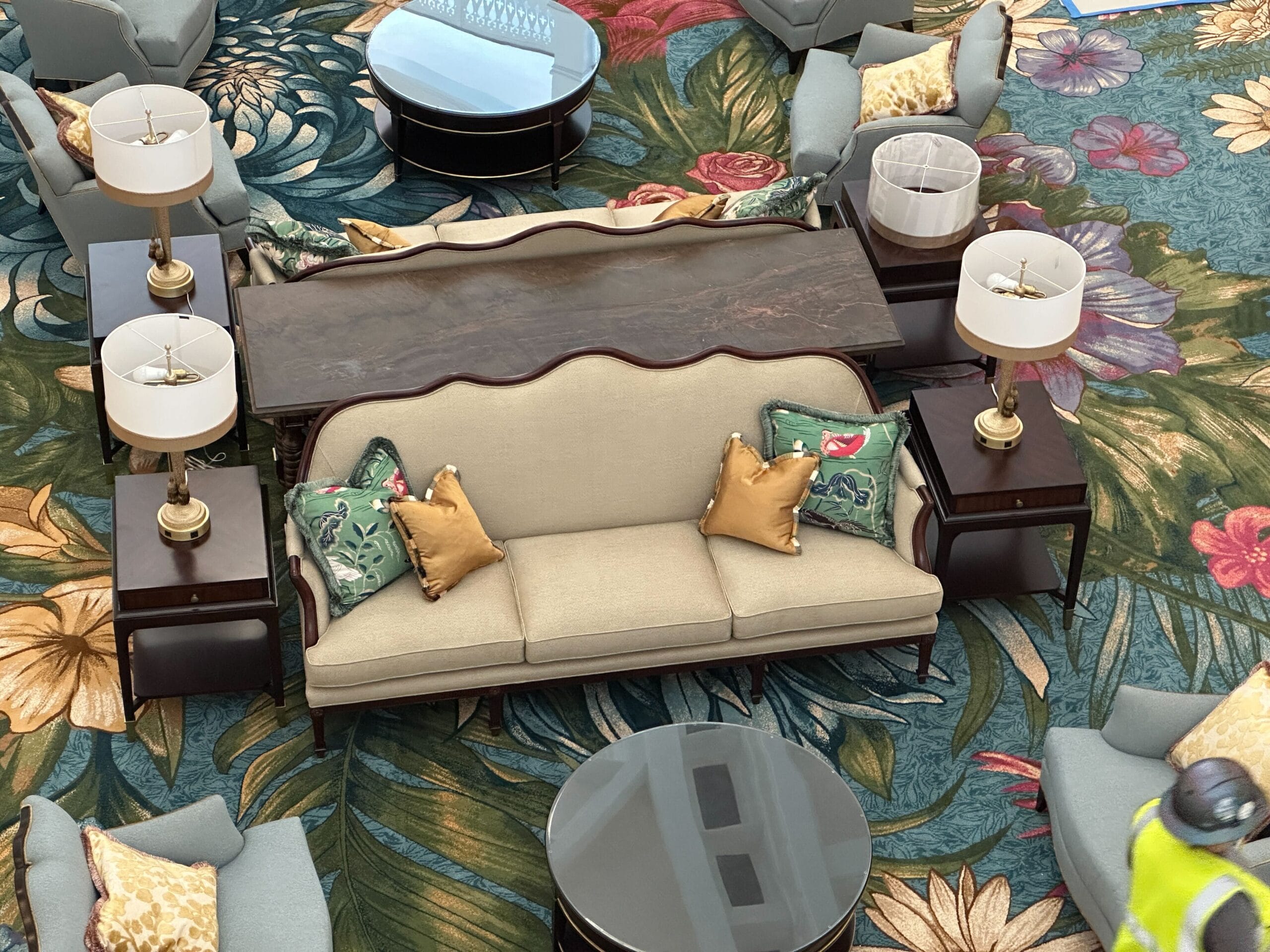 Beige sofa with floral cushions, Grand Floridian Resort-inspired lobby furniture, on a flowered carpet, classic Disney elegance.