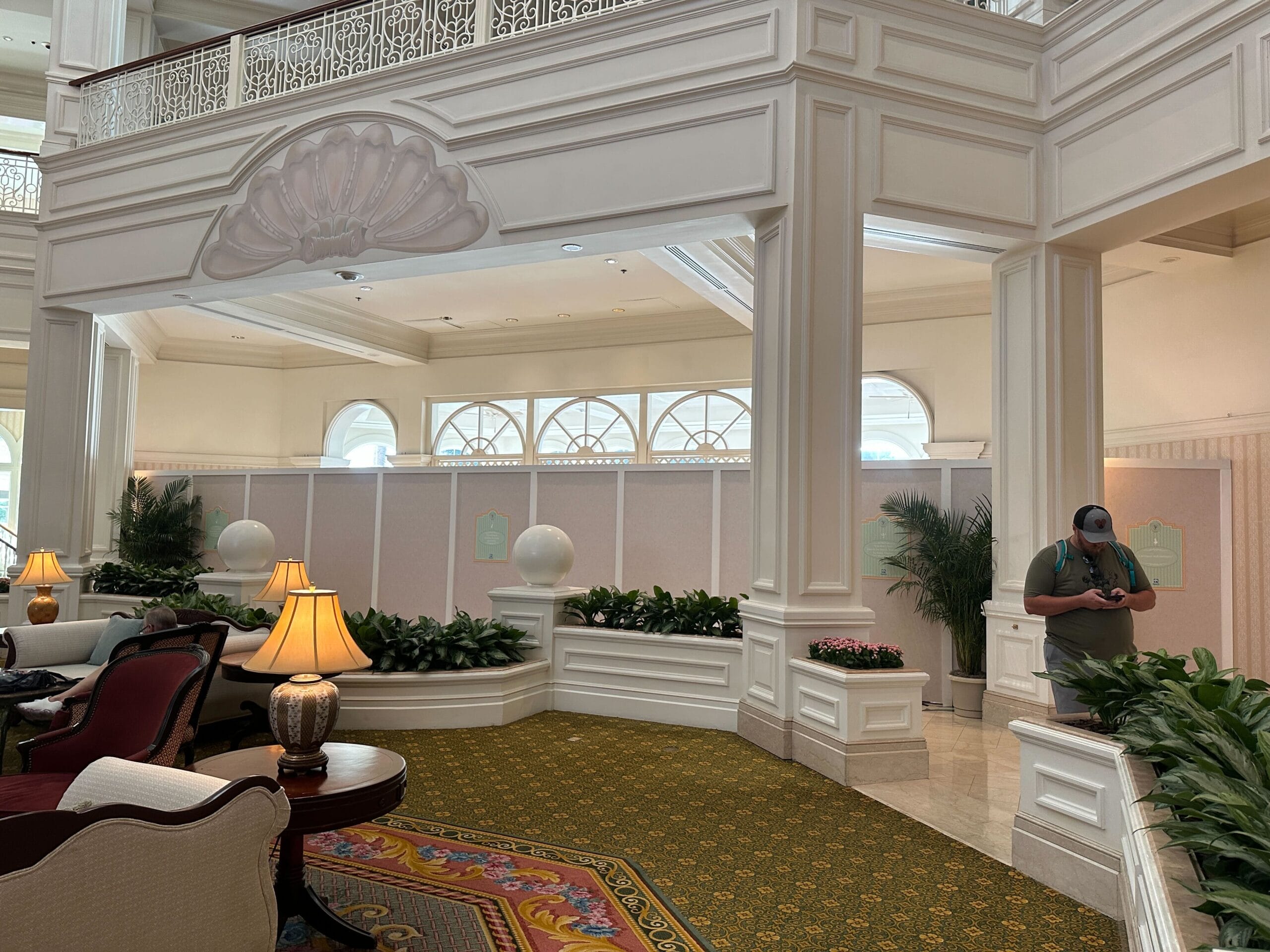 Elegant hotel lobby with white paneling, green carpet, lamps, and a person standing near a temporary construction wall.