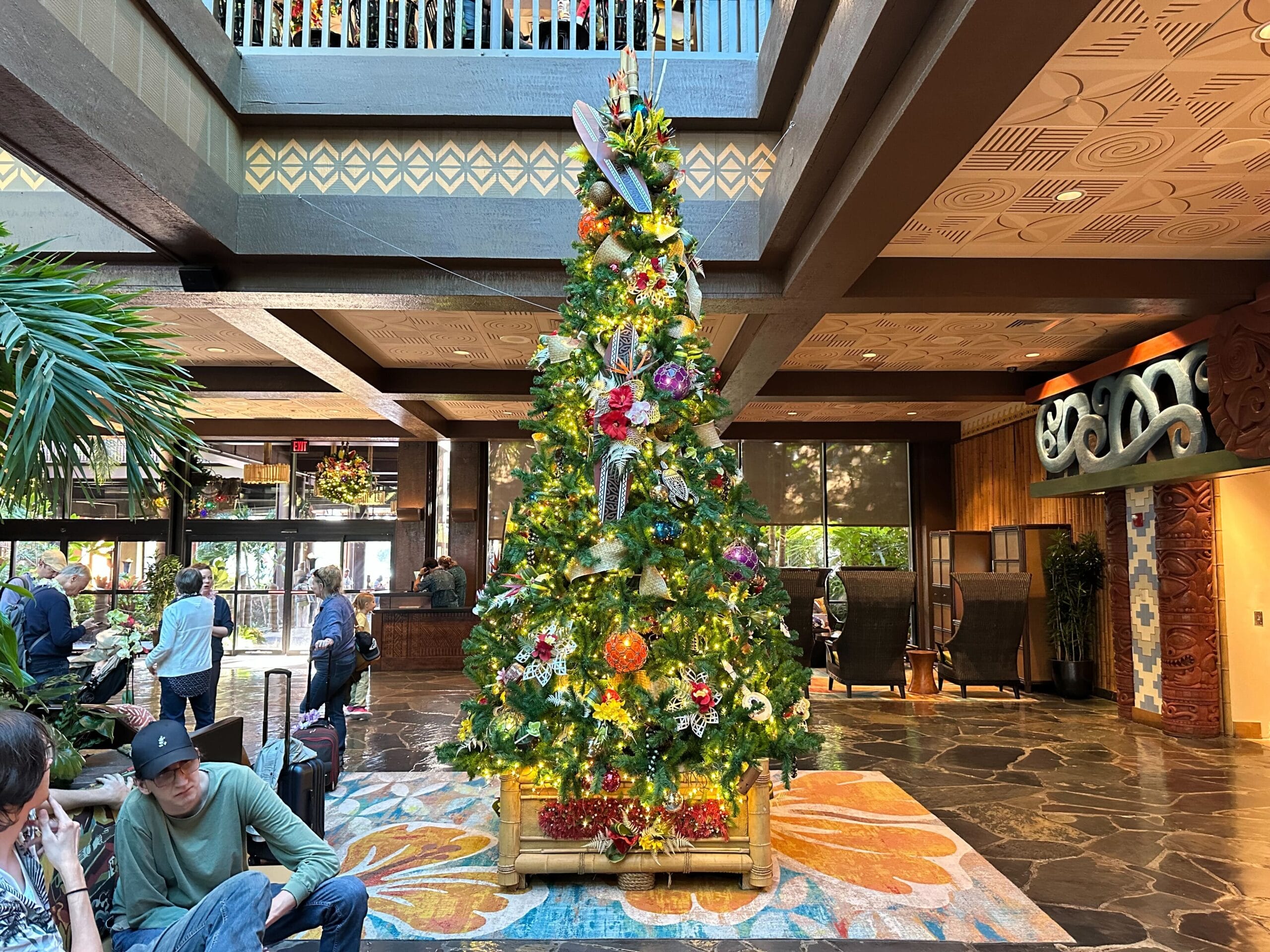 A decorated Christmas tree stands in a hotel lobby, surrounded by people.
