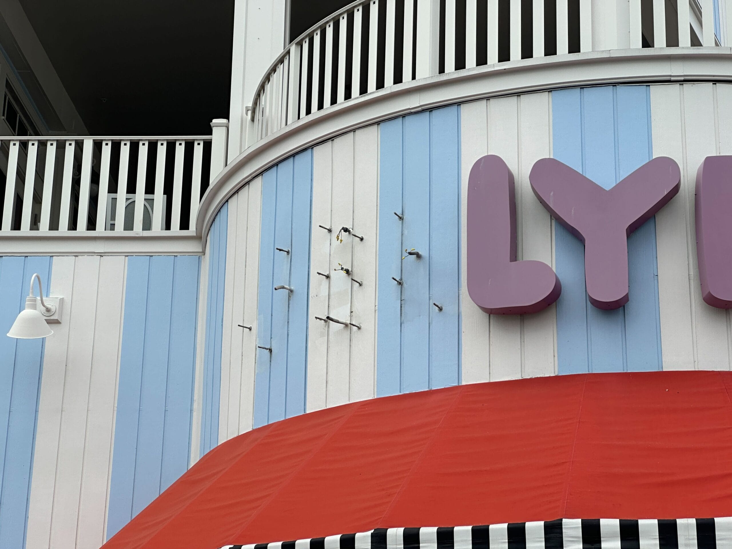 Pastel blue and white wall with missing sign letters, next to “LY,” above Jellyrolls’ red awning and black-striped trim.