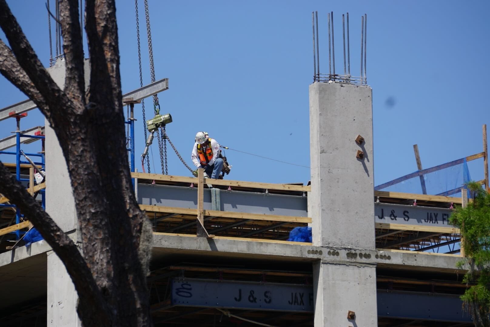 A construction worker in safety gear kneels on an unfinished Disney building structure under a clear blue sky, with reinforcing bars and wooden supports clearly visible, offering a dynamic construction update.