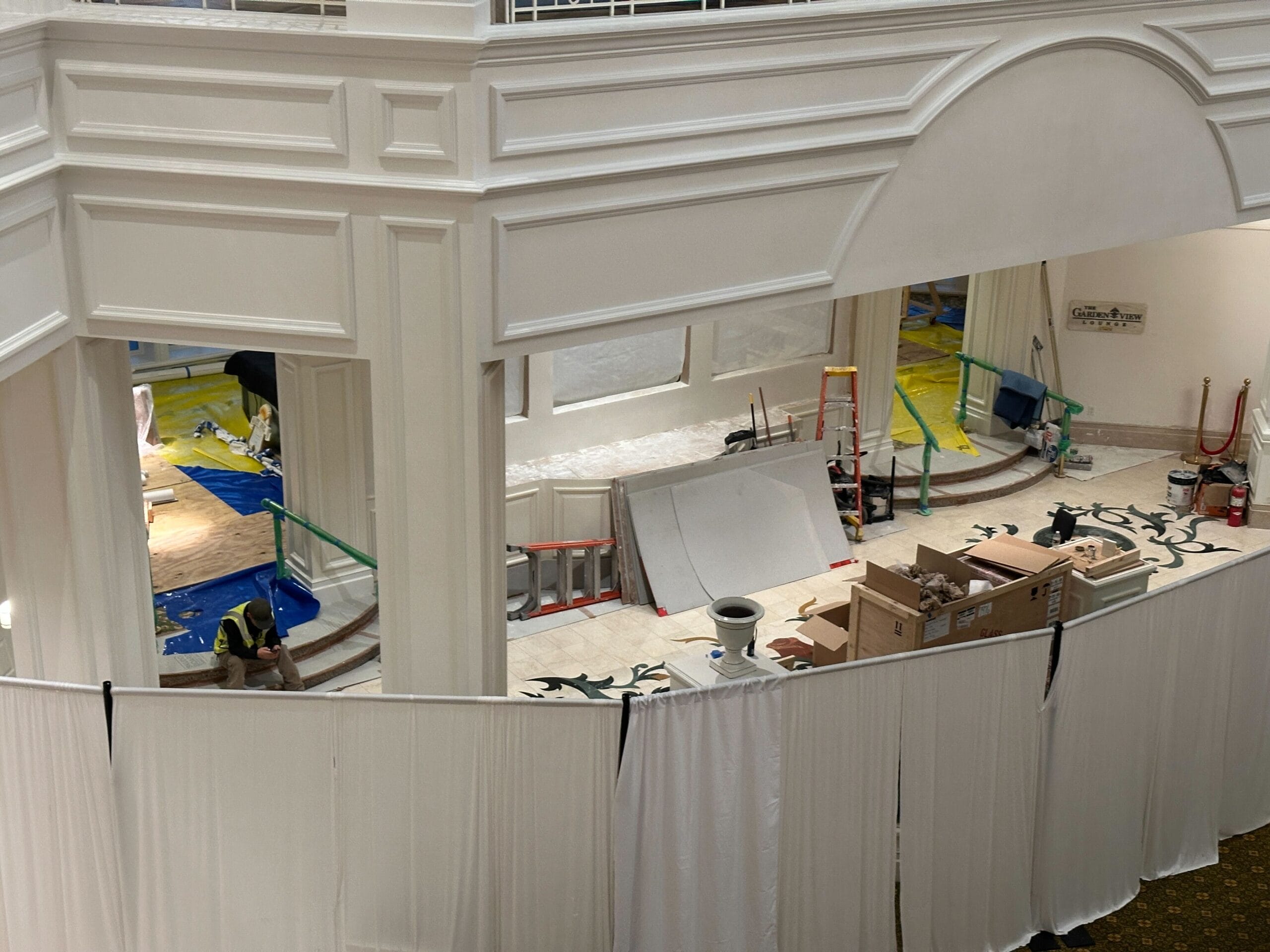 Construction area inside a building, with tools, boxes, ladders, and white curtains blocking the view.