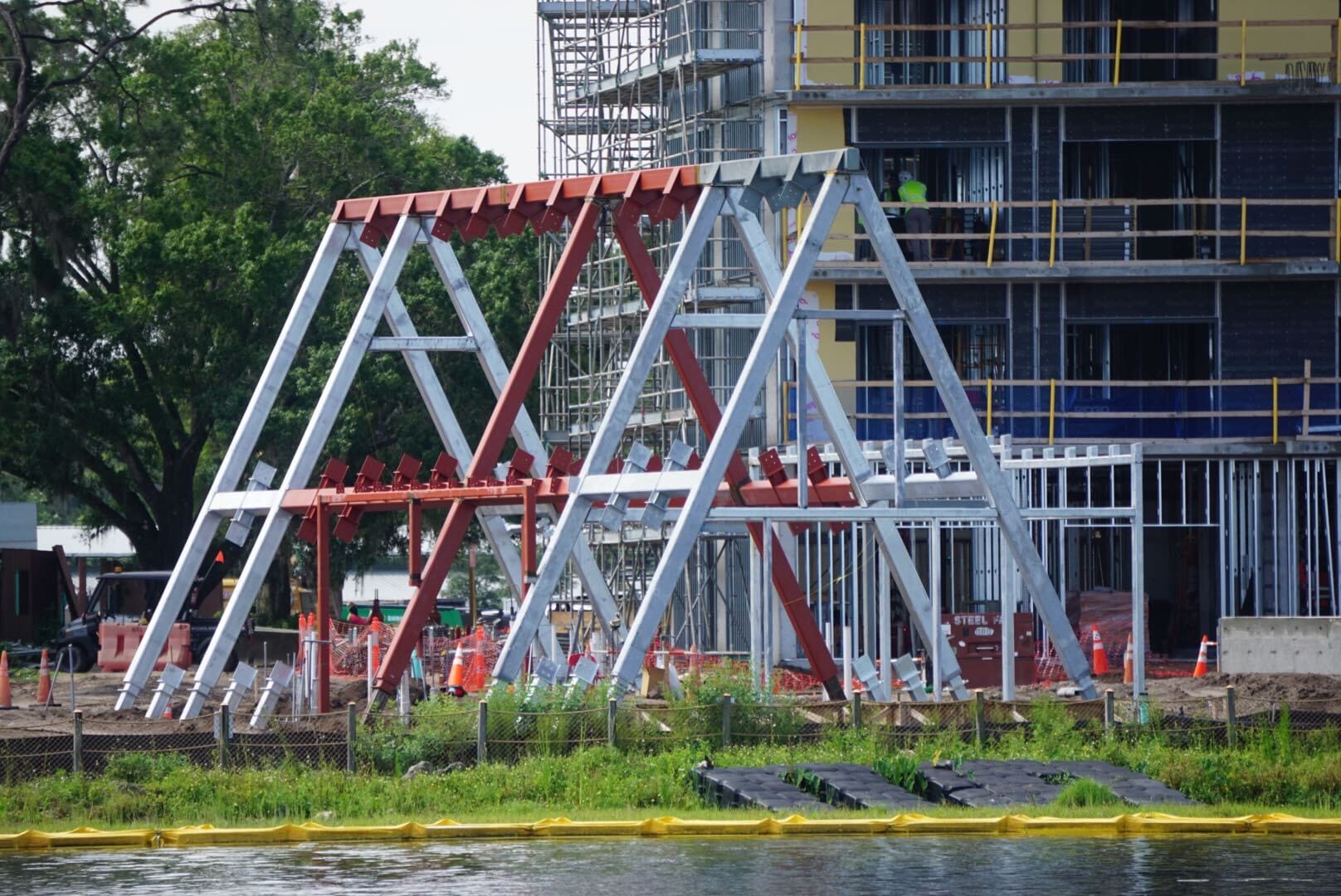 Red and white metal A-frame structures stand near a construction site by the water, with a building in the background.