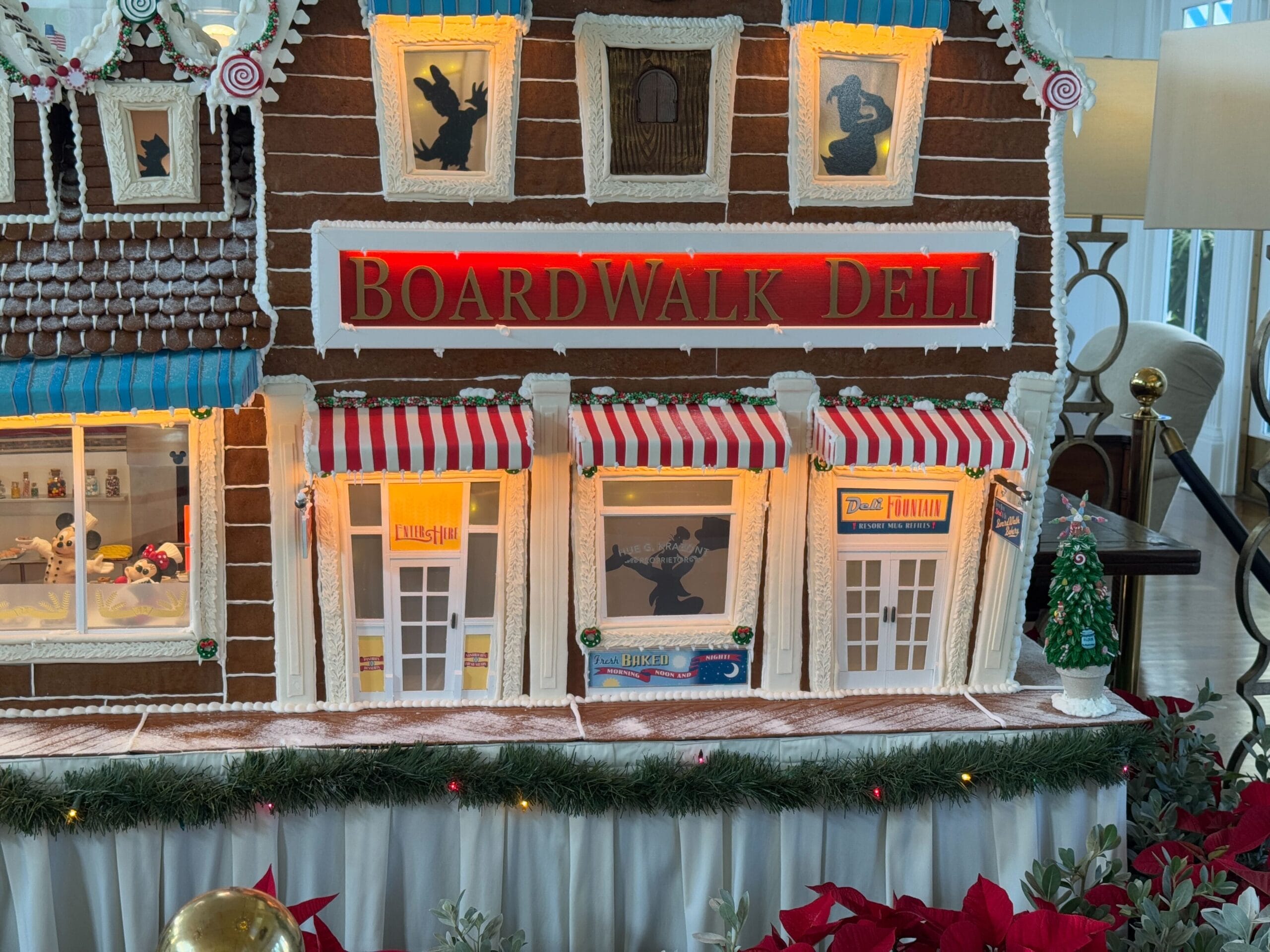 Gingerbread house depicting a deli with striped awnings, holiday decorations, and illuminated windows.