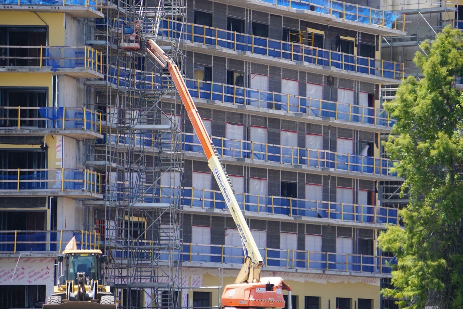 Construction site with a multi-story building, scaffolding, and a cherry picker lift near the structure.