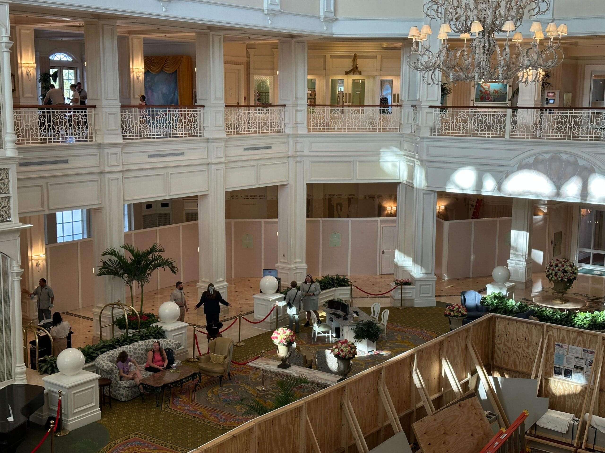 A hotel lobby with construction barriers, plants, seating, people, and h2o glow after hours food available nearby.