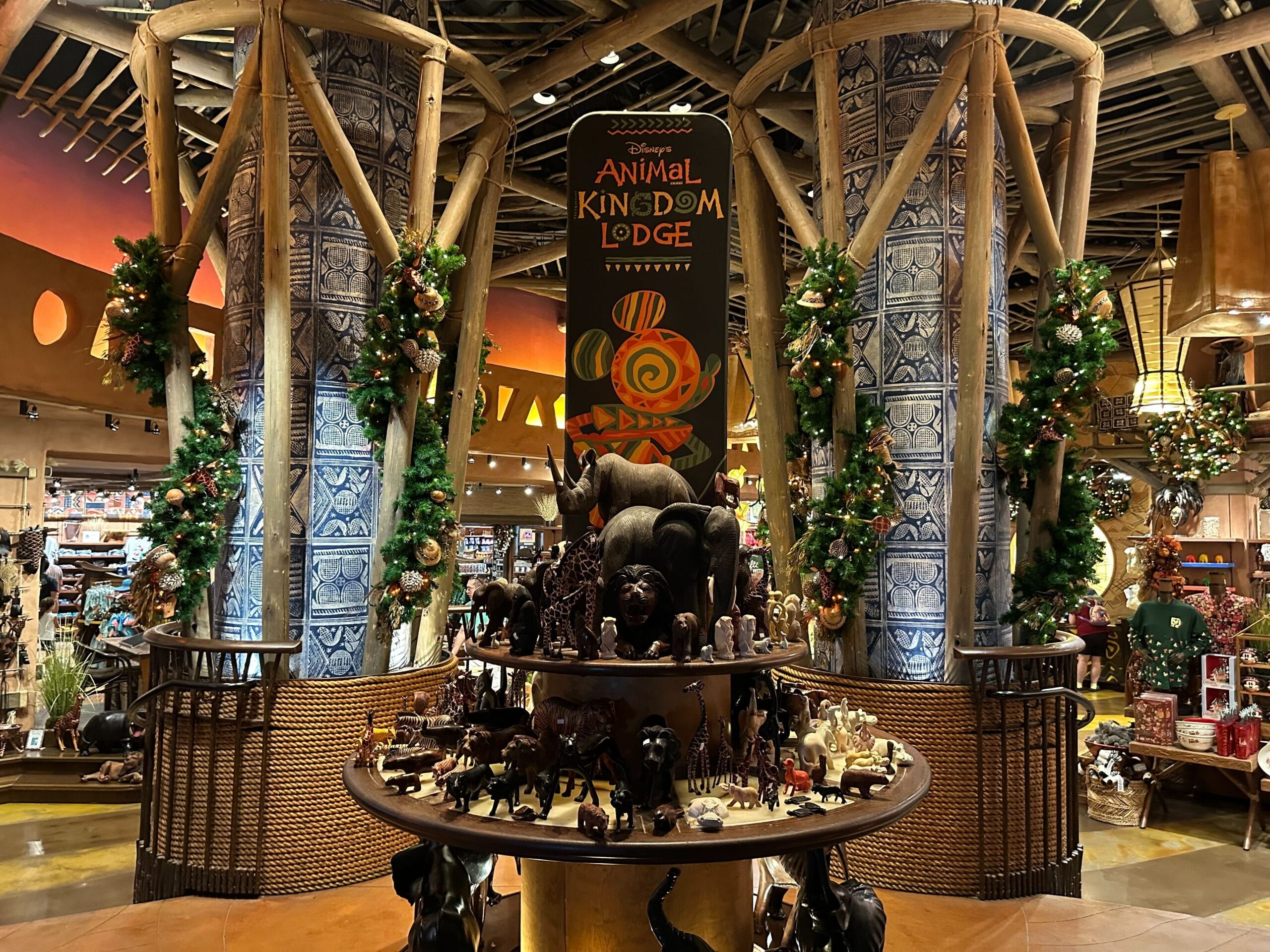 A display of African animal figurines is arranged under a Disney's Animal Kingdom Lodge sign, surrounded by decorated pillars and holiday garlands.