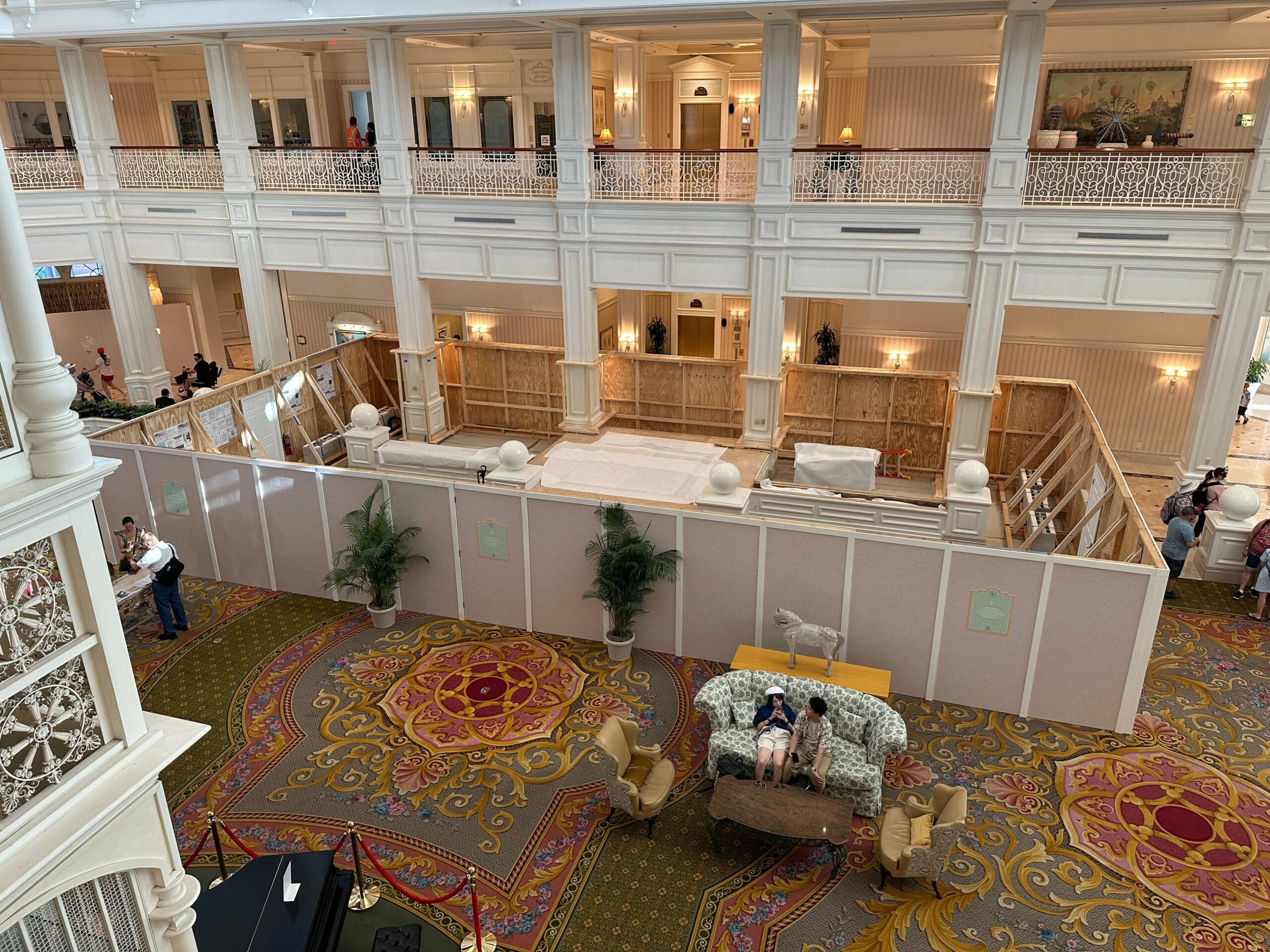 Hotel lobby with ornate carpet and furniture; a large construction area is enclosed by temporary wooden walls.
