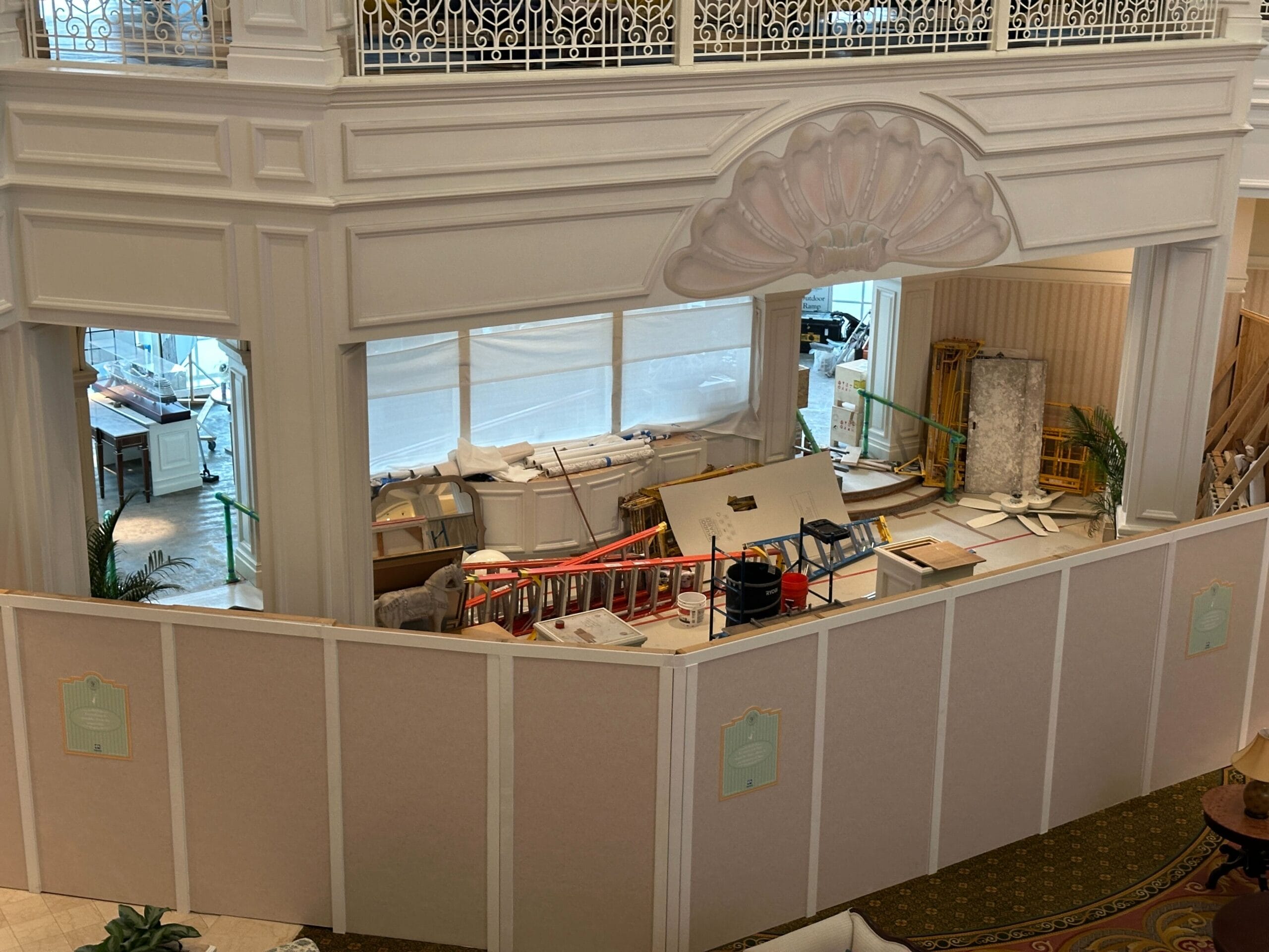 Construction area in a large hotel lobby, with barriers, tools, and materials behind a decorative shell-shaped arch.