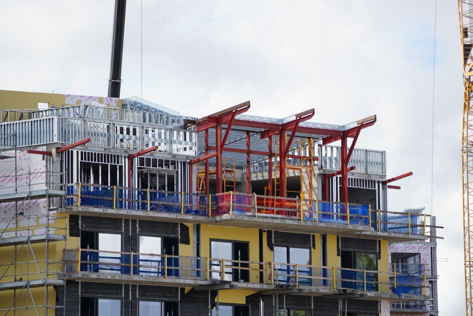 A building under construction with steel beams, scaffolding, and yellow insulation visible on the upper floors.