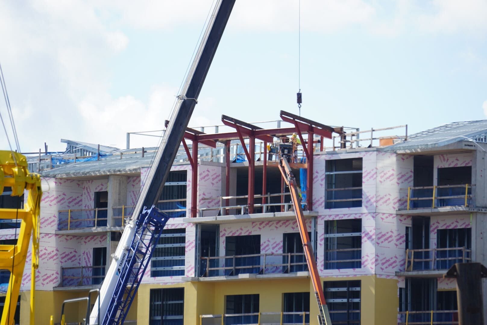 Construction workers on lifts build the upper floors of Disney Lakeshore Lodge amid cranes and scaffolding.