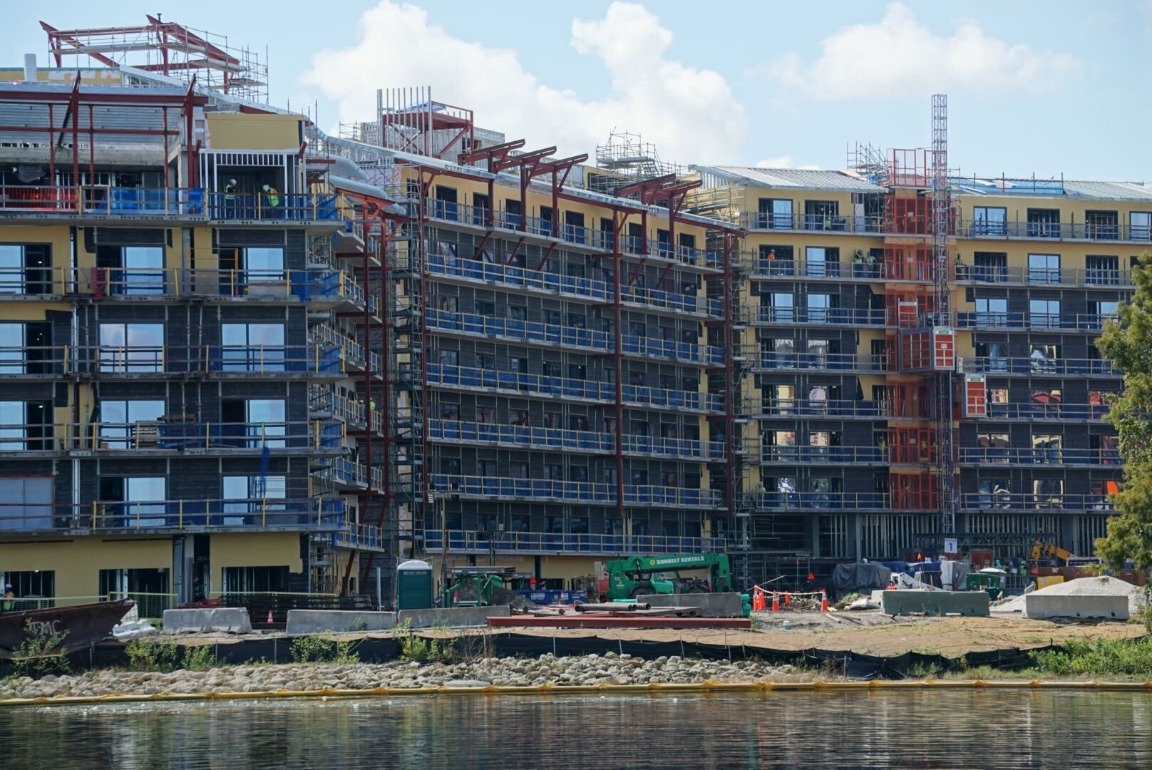 A multi-story Disney Lakeshore Lodge is under construction by the waterfront, with scaffolding and equipment visible.