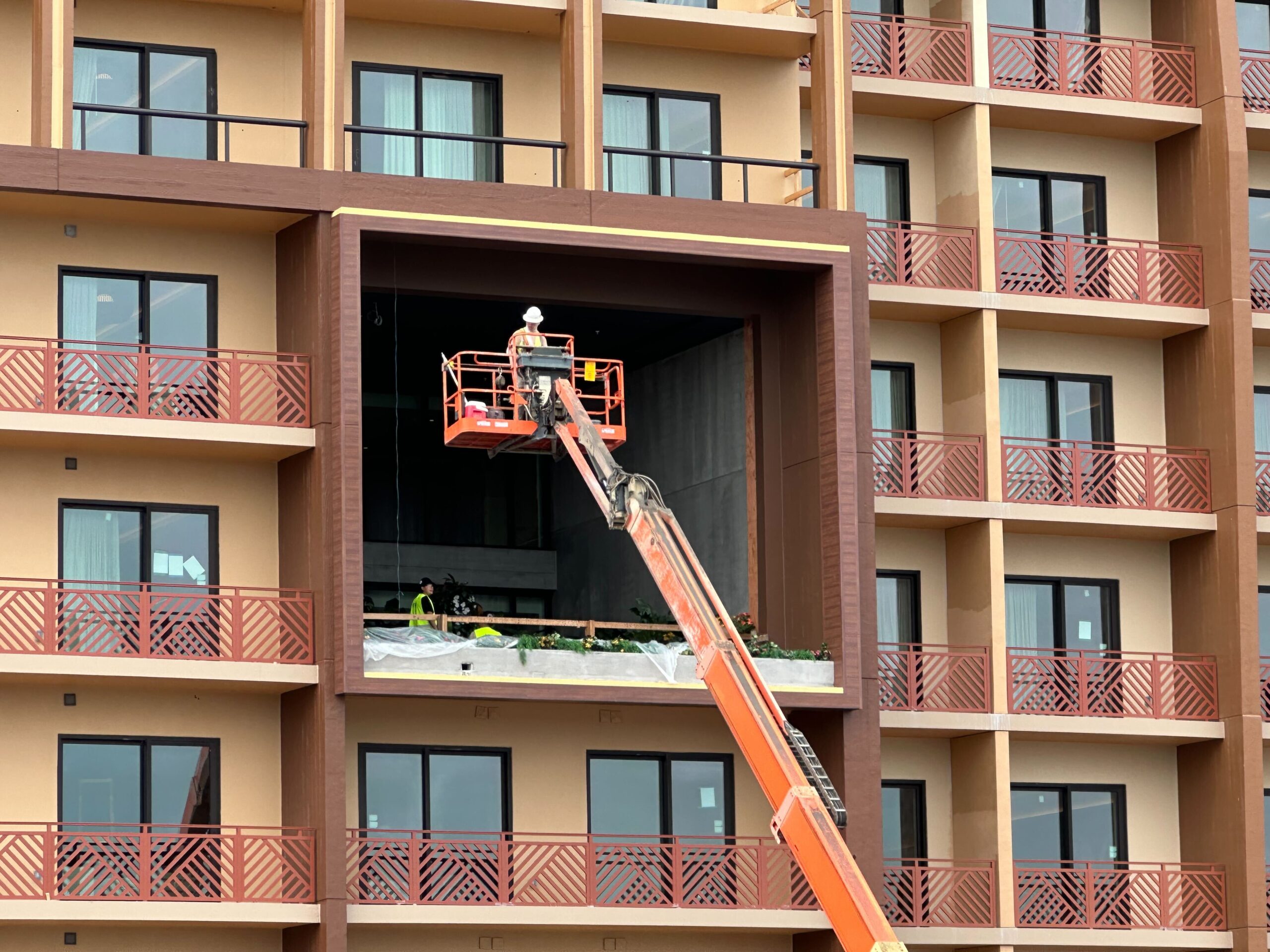 A construction worker on a lift working on the exterior of a multi-story building, with a large opening under construction.