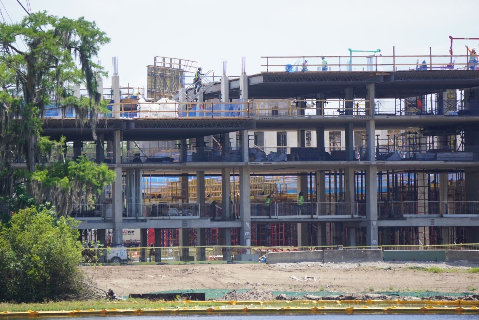 A multi-story building under construction with scaffolding and equipment visible. Partial greenery is in the foreground.