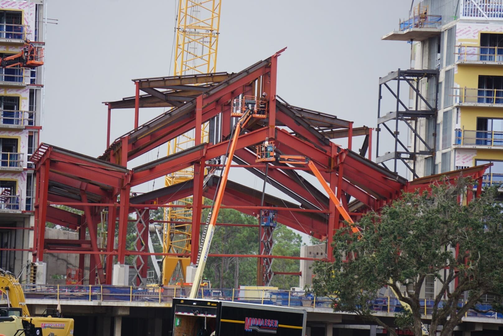Red steel beams shape Lakeshore Lodge's frame, with cranes and unfinished structures marking ongoing construction updates.
