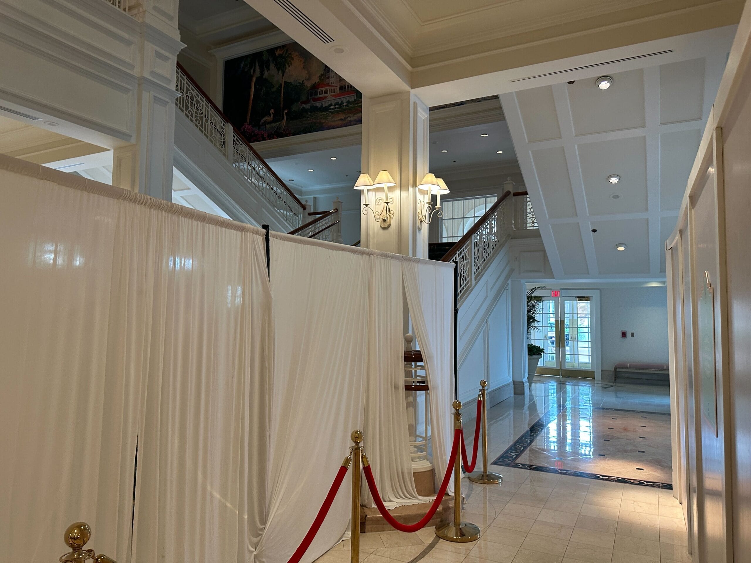 White curtains and red ropes section off part of an elegant hotel lobby with stairs and marble floors.