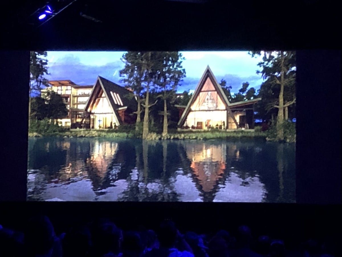 A projected image shows Lakeshore Lodge Construction’s A-frame houses by a lake, trees reflecting in dusk water.