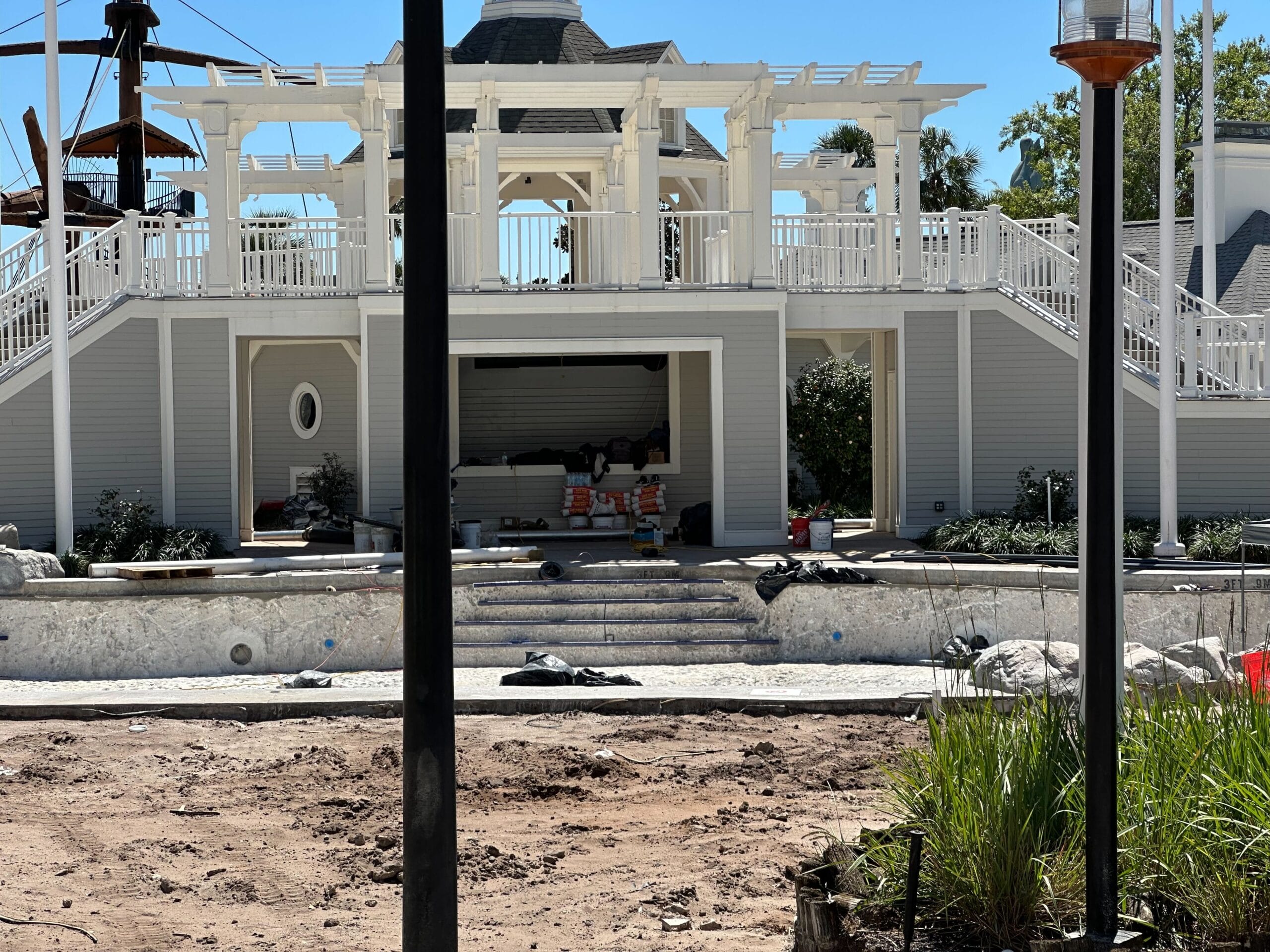 A building under construction stands beside the Stormalong Bay Pool, with a foreground of dirt and construction materials. Steps and a white pergola lead to the entrance of Disney's Yacht Club, seamlessly blending luxury with progress.