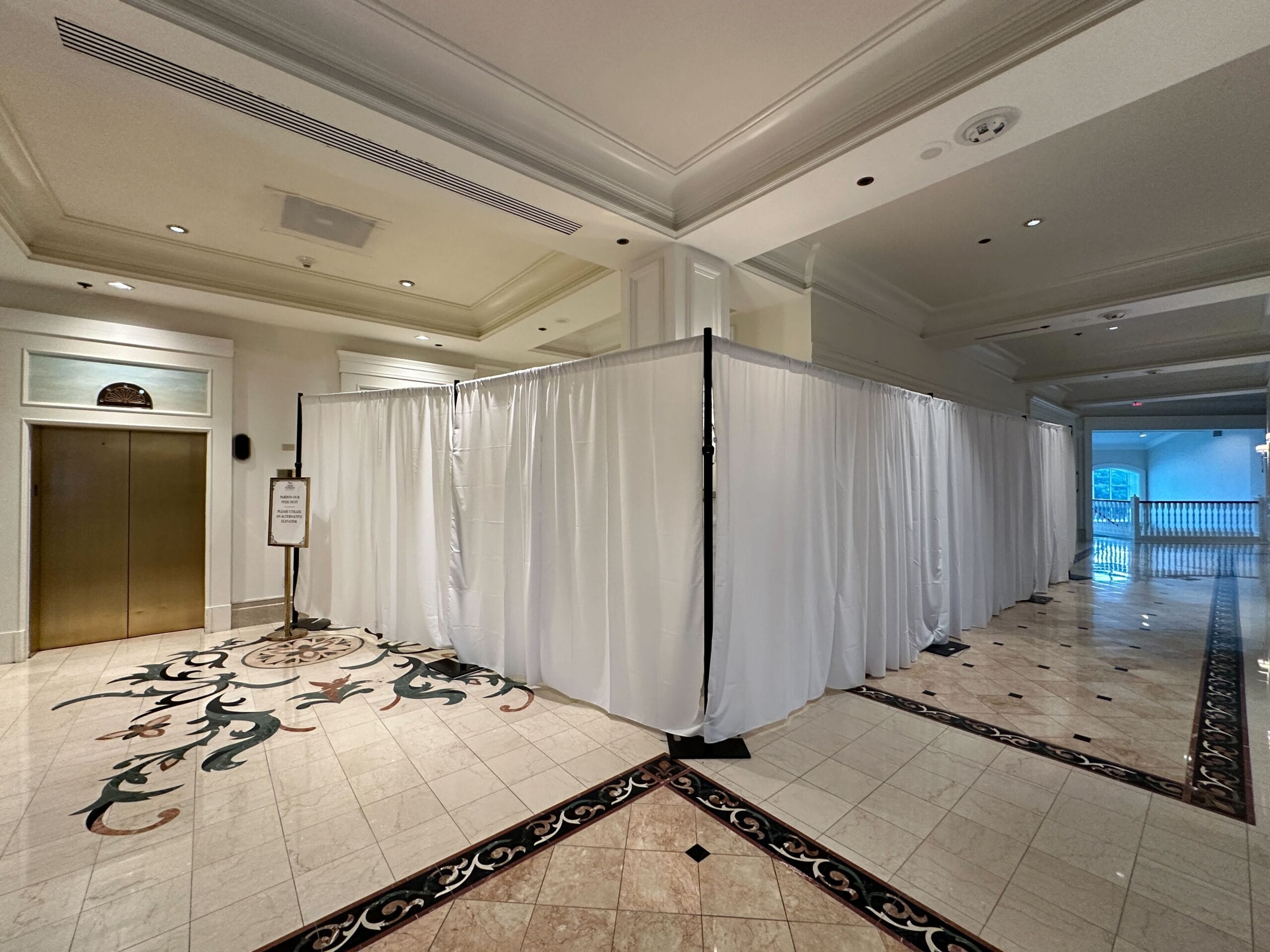 White curtains form a temporary enclosure in a hotel hallway near an elevator and a decorative tile floor.