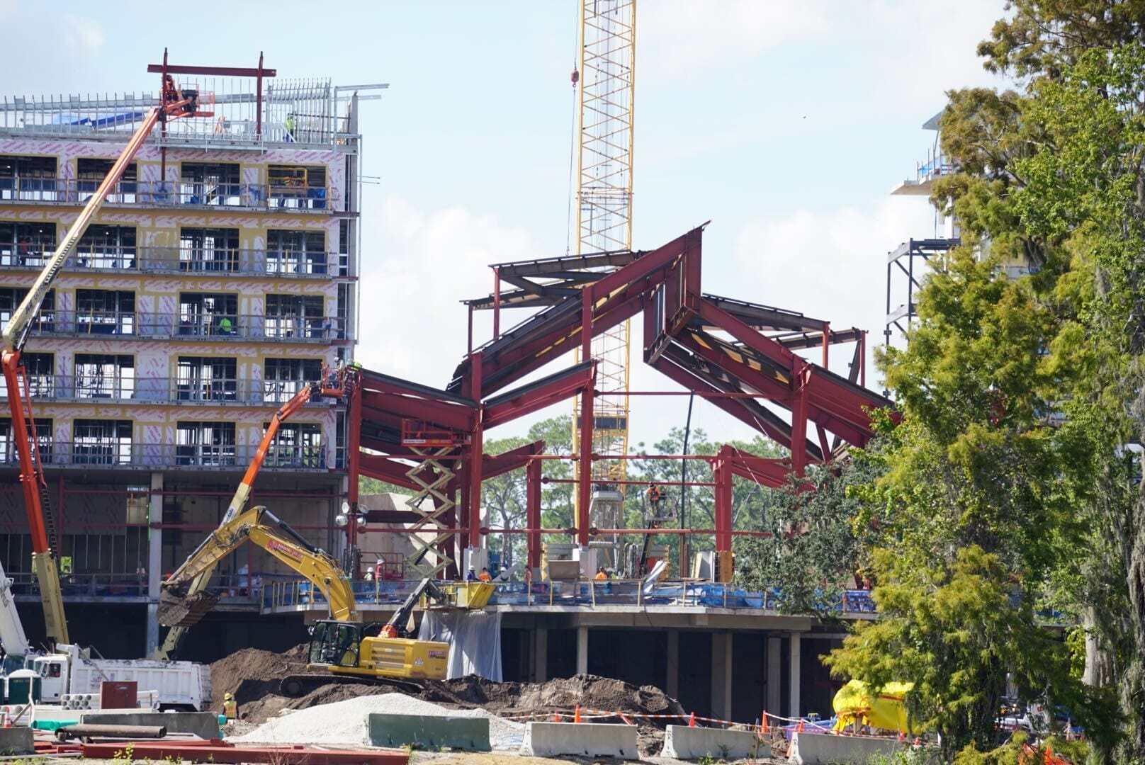 Steel framework and cranes at Disney Lakeshore Lodge construction site with a multi-story building in the background.