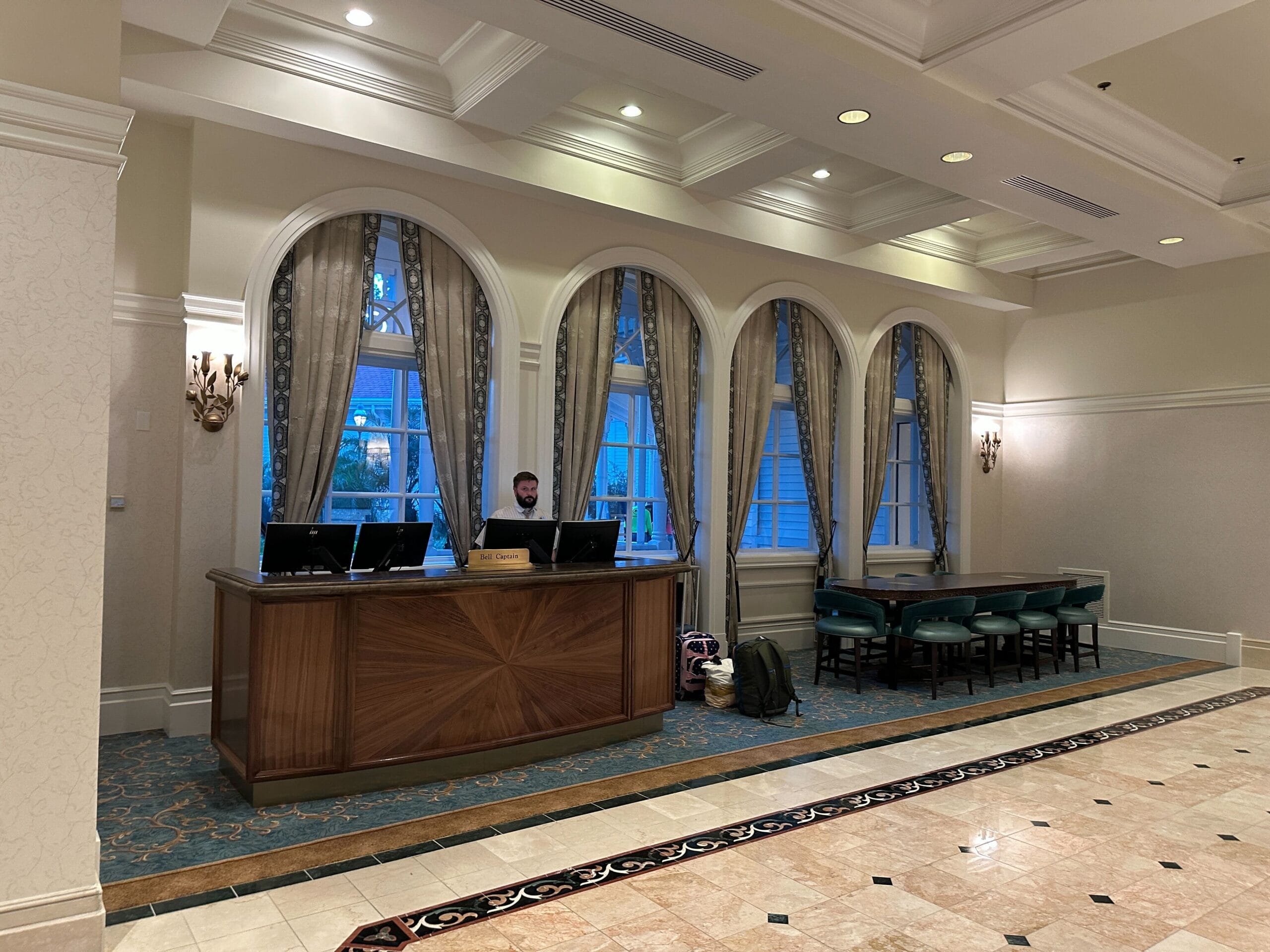 Hotel lobby at the Grand Floridian with a person at a wooden front desk and green chairs by tall windows.