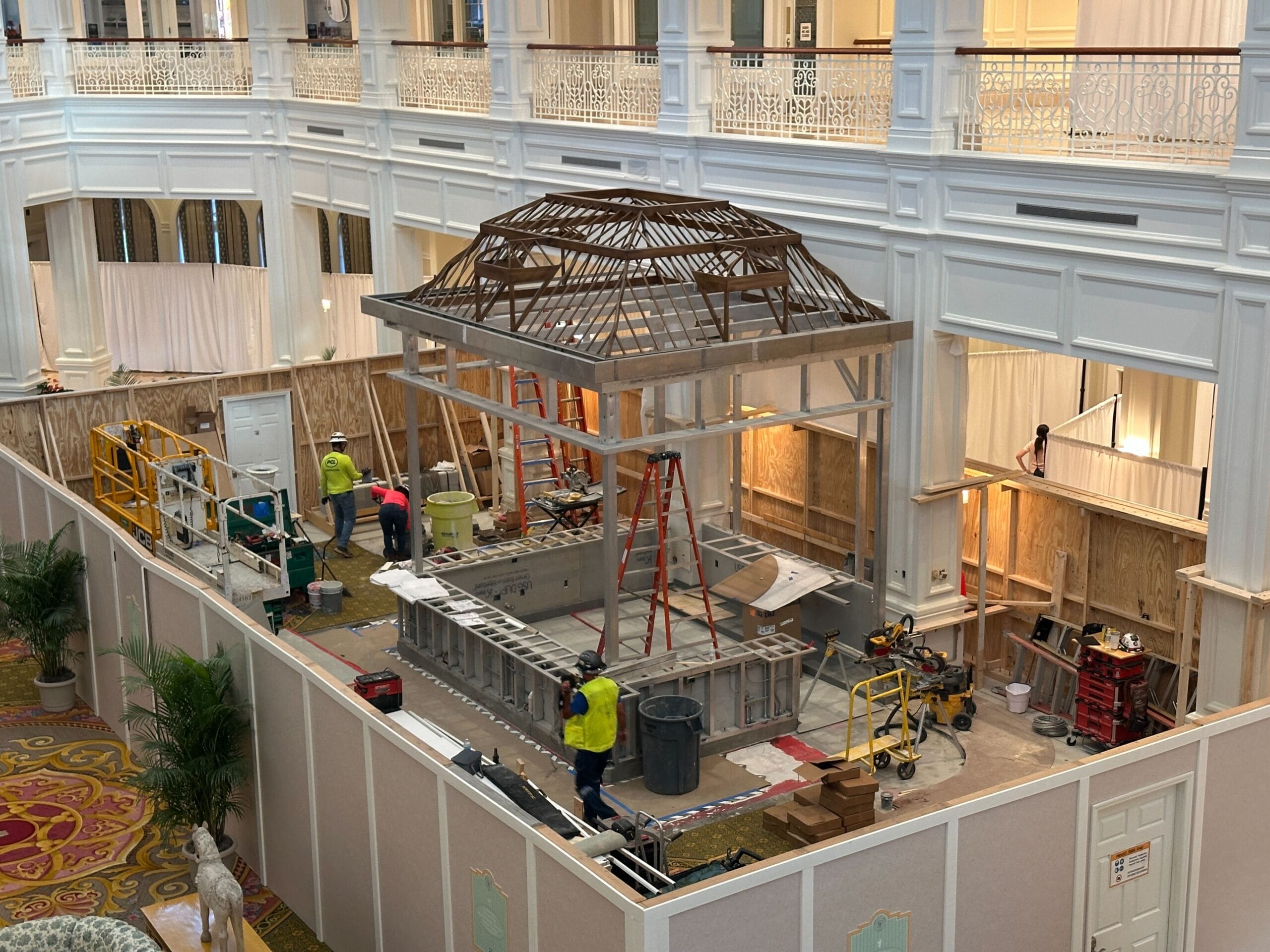 Workers construct a large indoor structure with scaffolding and wood beams in a grand, ornate hotel lobby.