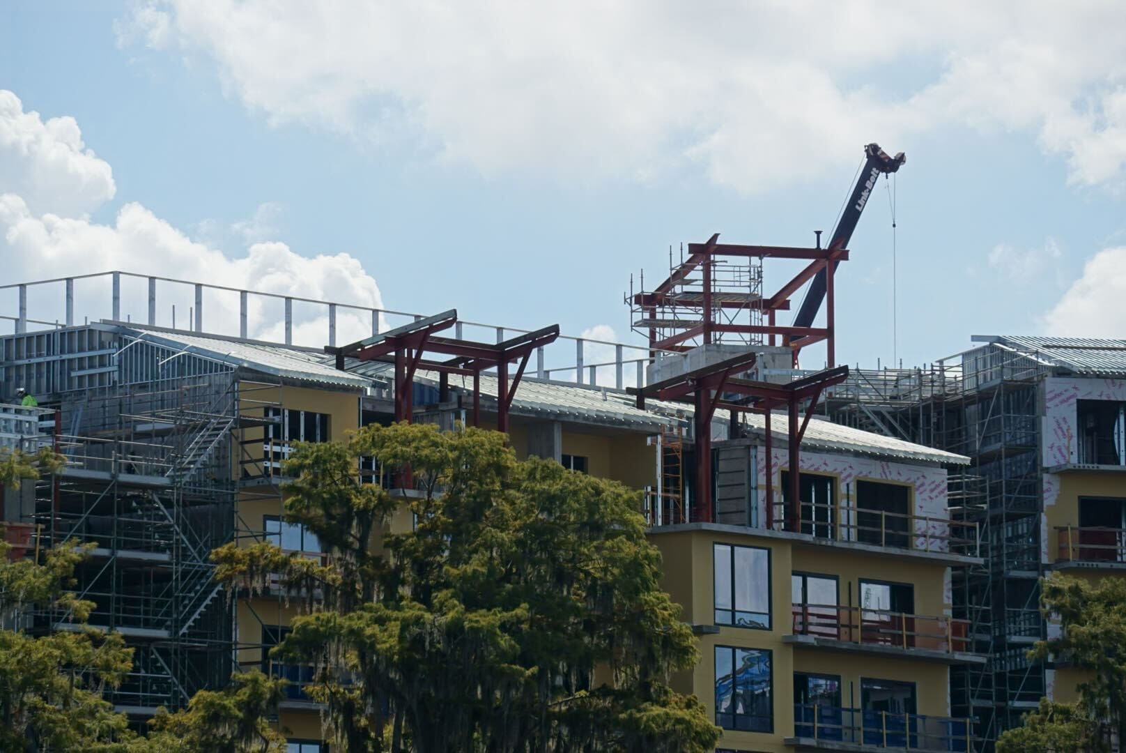 Several buildings under construction at Disney Lakeshore Lodge with scaffolding, steel beams, and a crane under a cloudy sky.