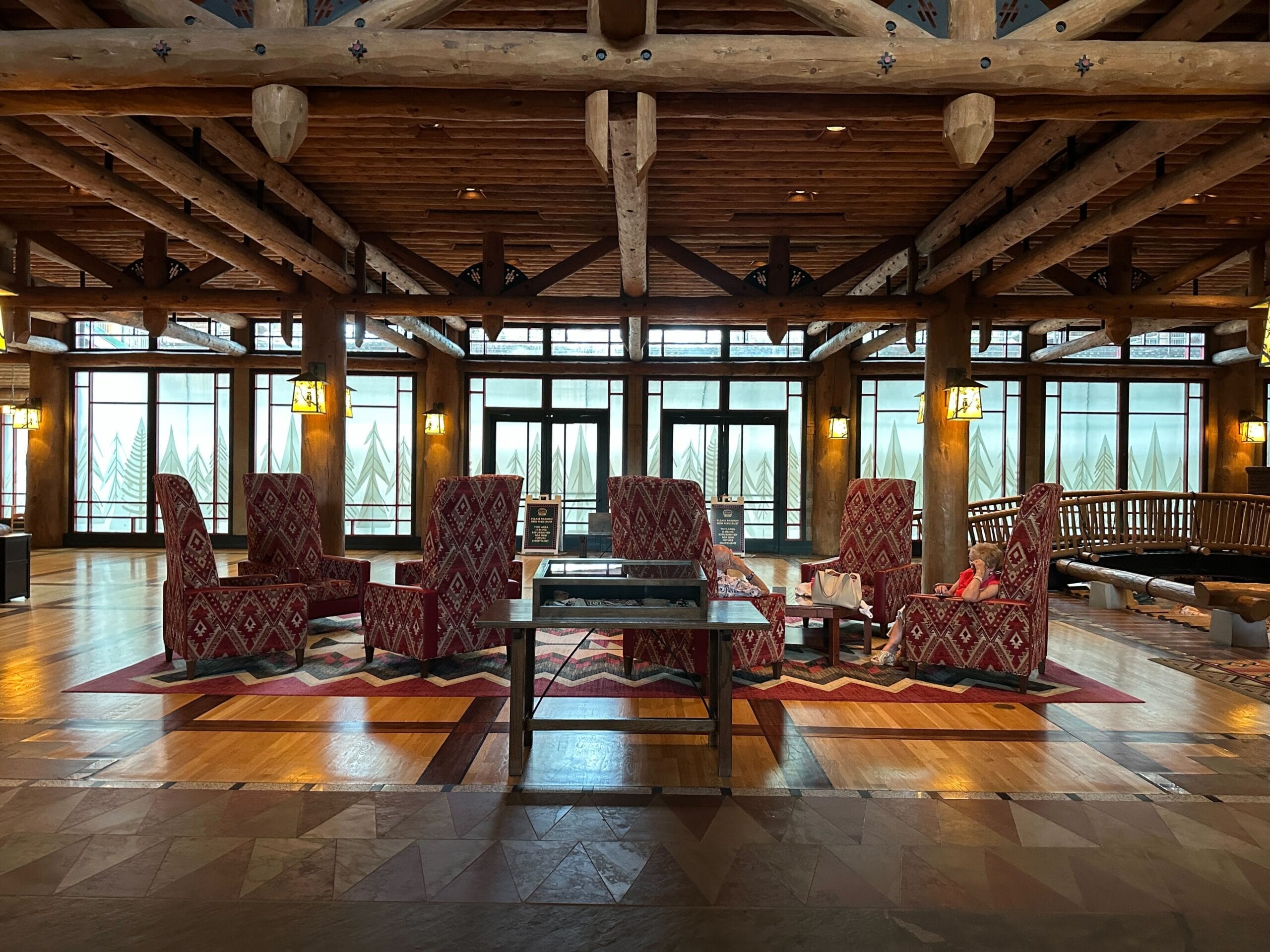 Cozy Fort Wilderness Lodge interior with patterned chairs, wood beams overhead, and large windows in the background.