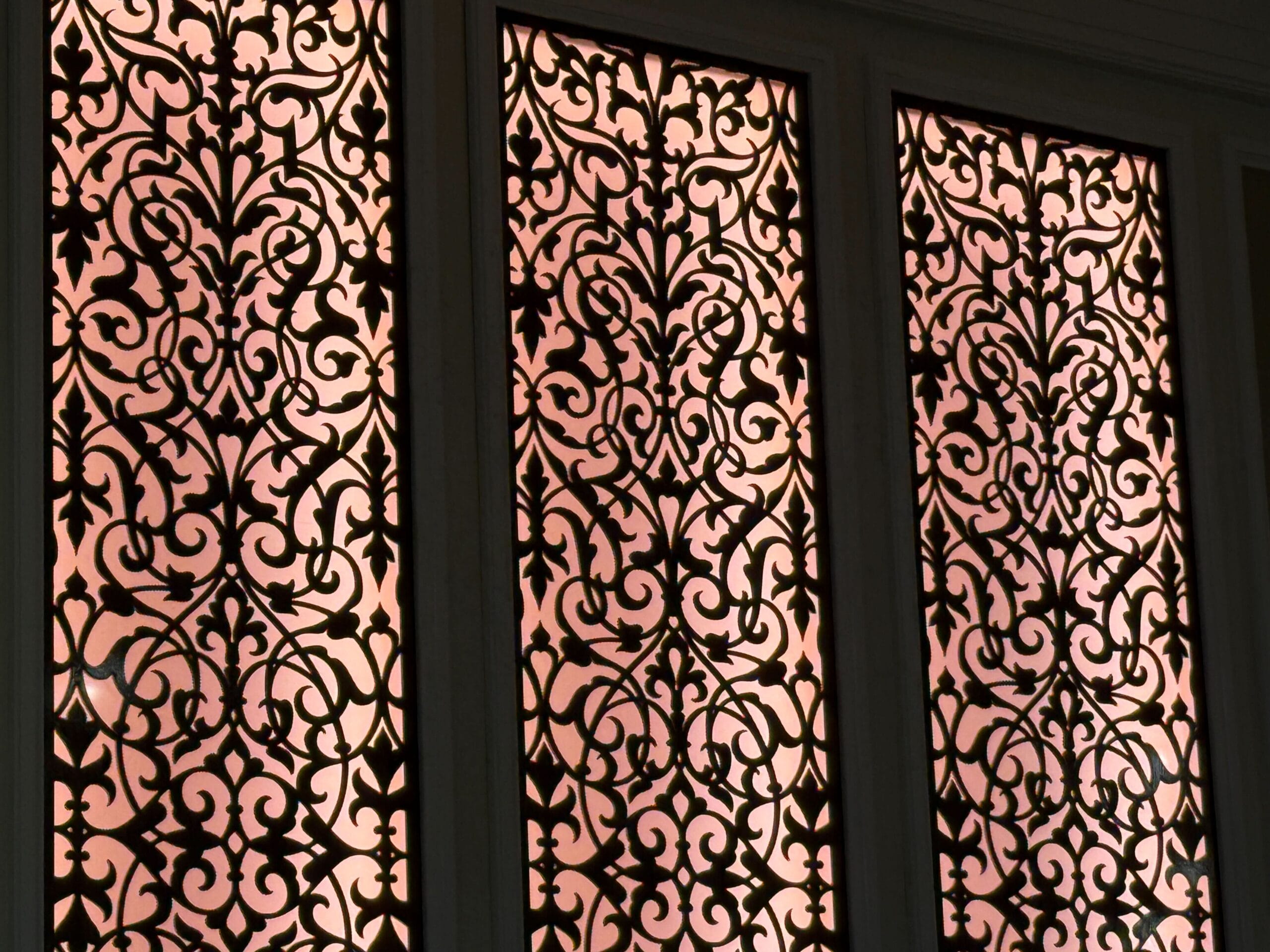 Ornate, intricate black metal window grilles with floral patterns, backlit by warm natural light.