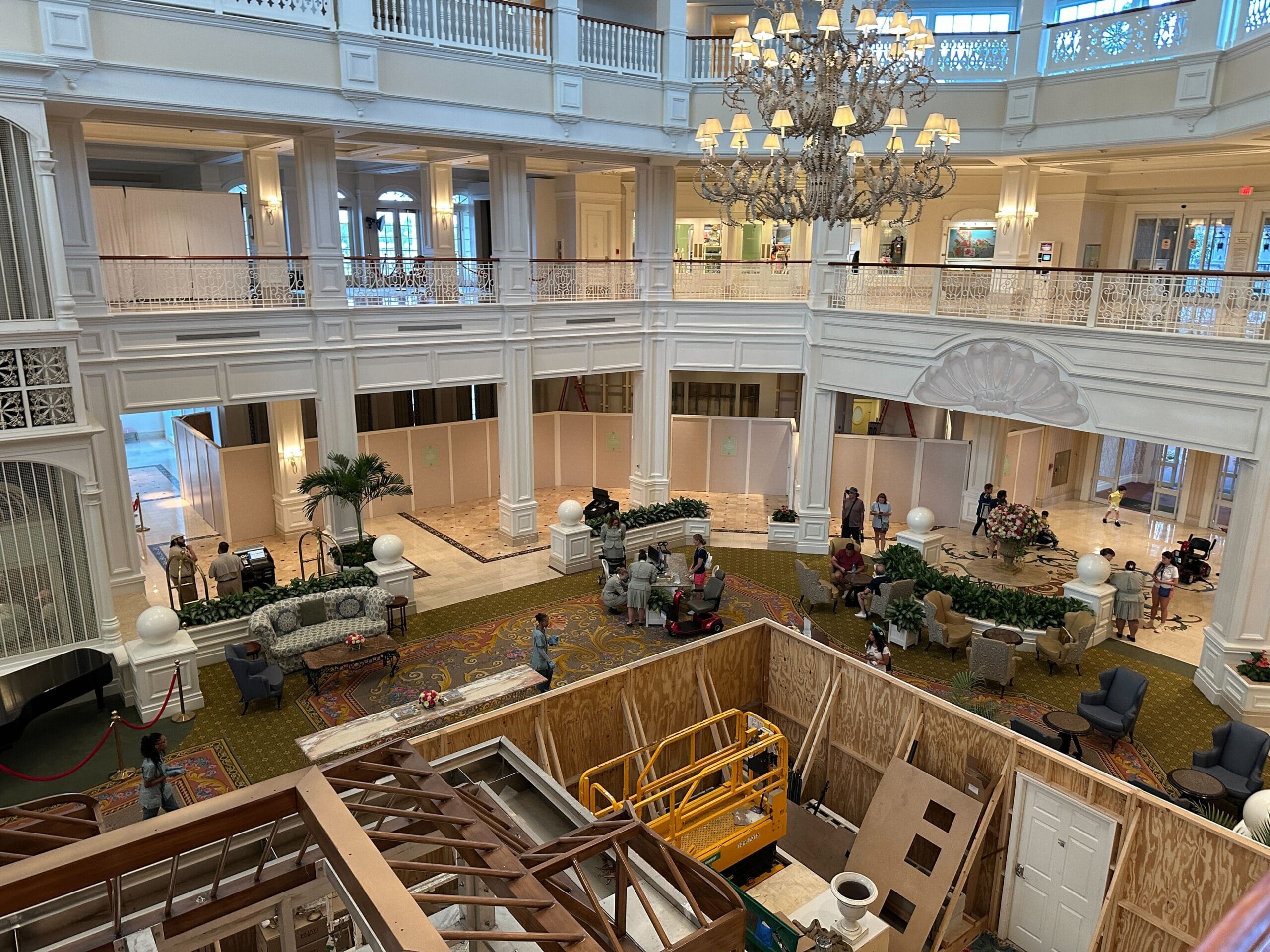 Grand hotel lobby with guests and furniture, and a large construction area with equipment in the center.