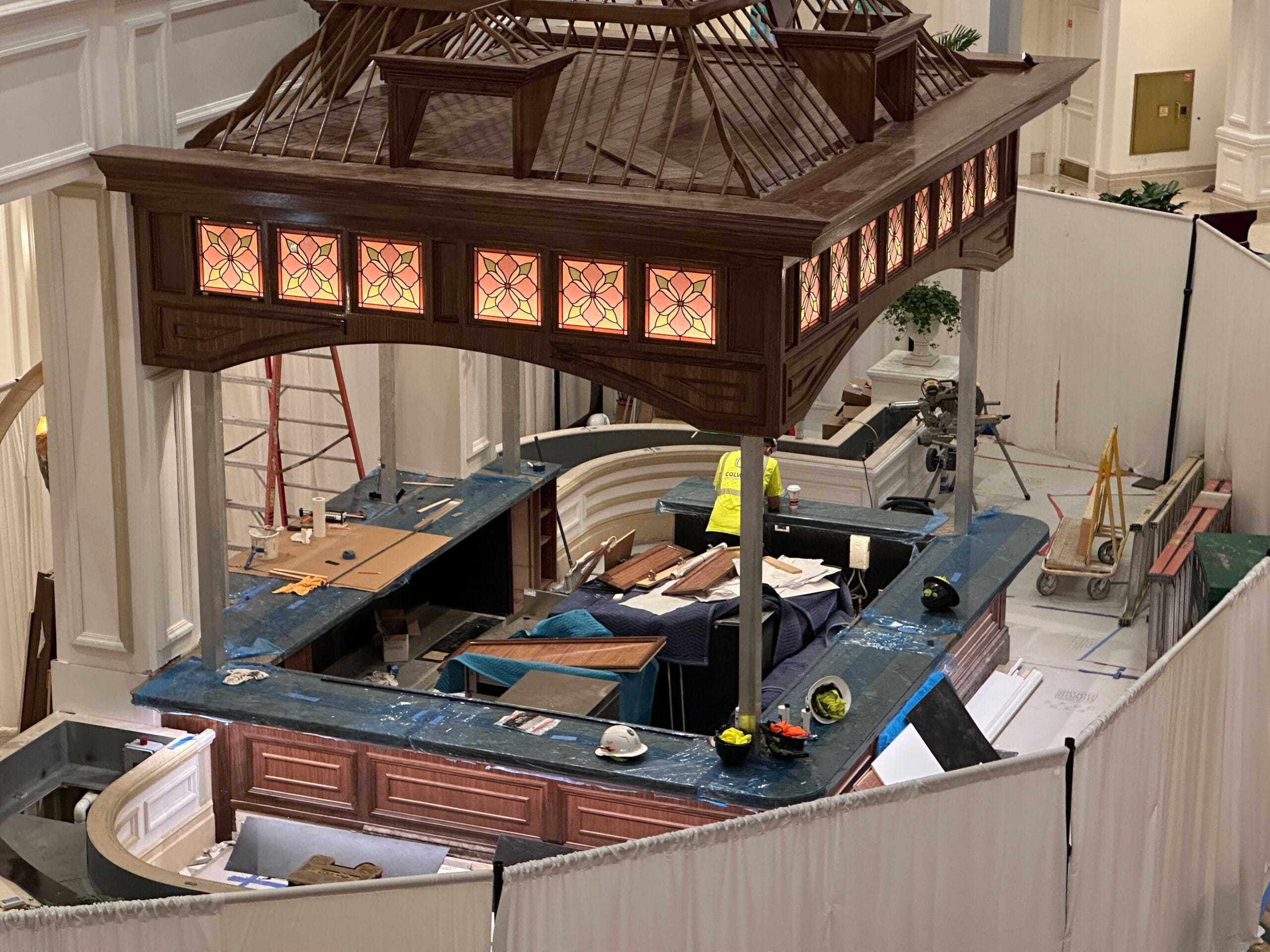 A partially constructed indoor bar with stained glass panels and countertops, resembling the theming seen in Disney park lounges.