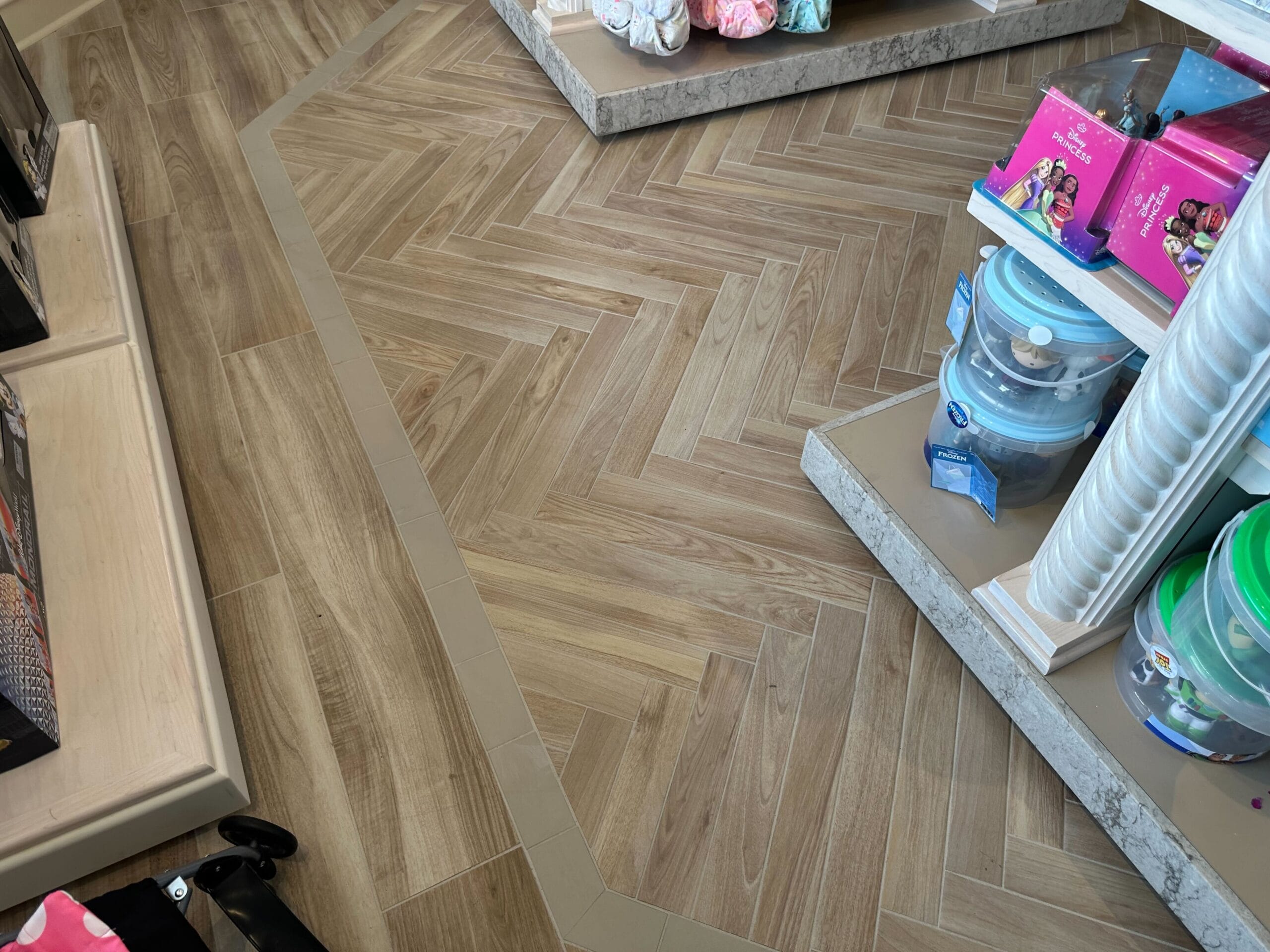 The recently renovated section features a herringbone-patterned wooden floor with a tile border, reminiscent of Disney's Boardwalk Inn. This aisle in the Screen Door General Store proudly showcases shelves filled with toys and containers.