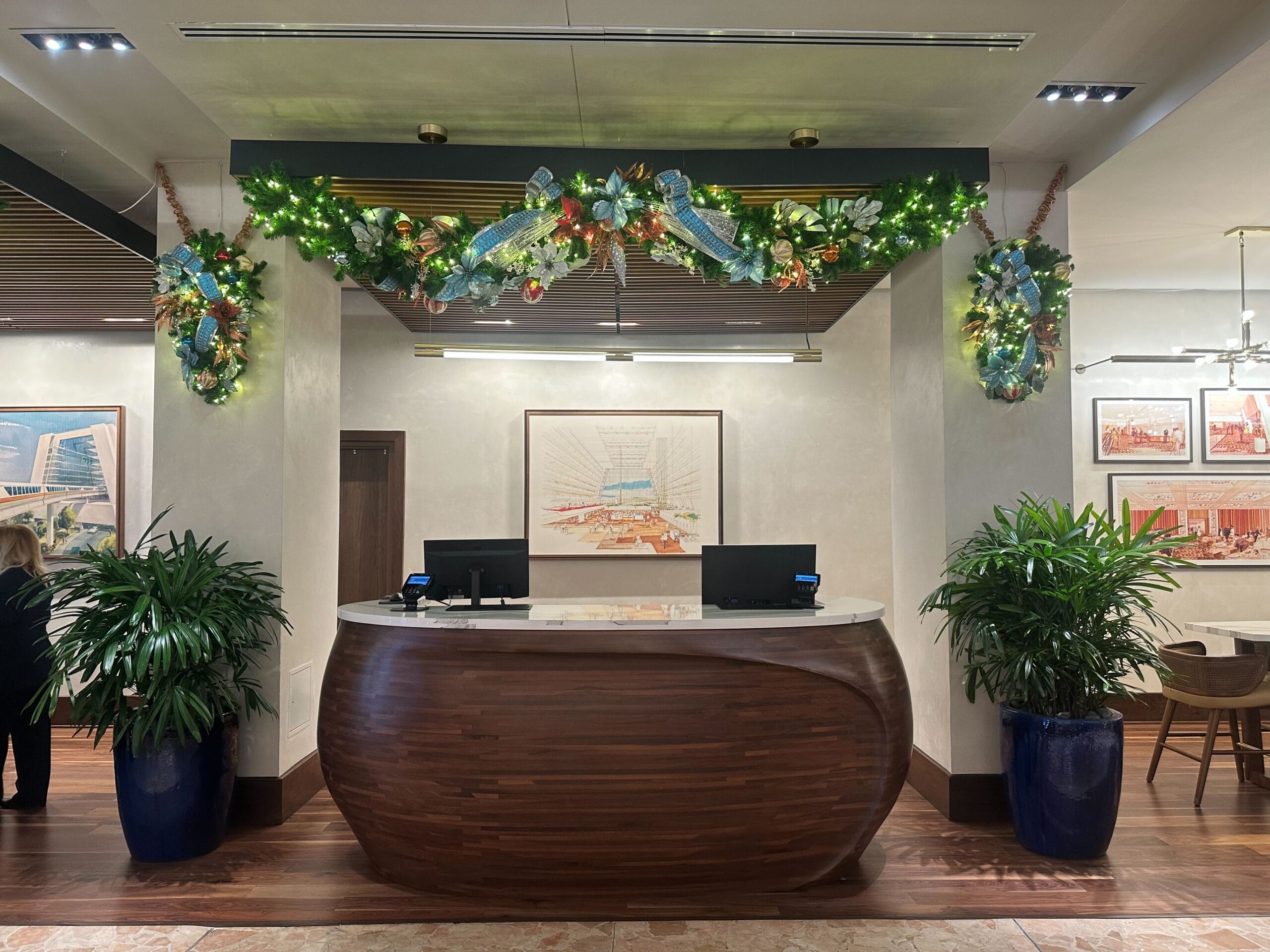 Hotel reception desk with wooden finish, decorated with holiday garland and greenery. Two computer monitors are on the desk, with framed artwork on the wall behind.