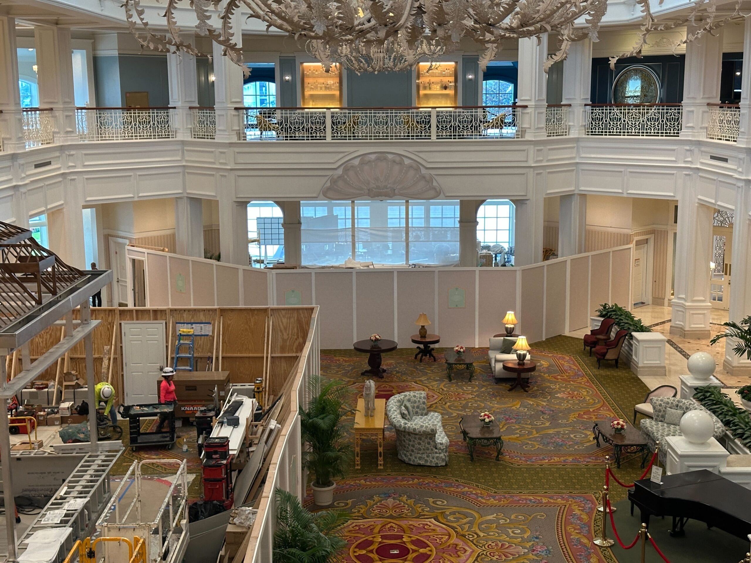 A hotel lobby with construction barriers and workers, alongside arranged furniture and decorative lighting.