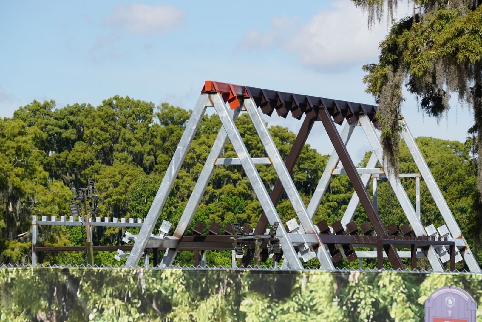 Triangular metal framework under construction at Disney Lakeshore Lodge, with trees and blue sky in the background.