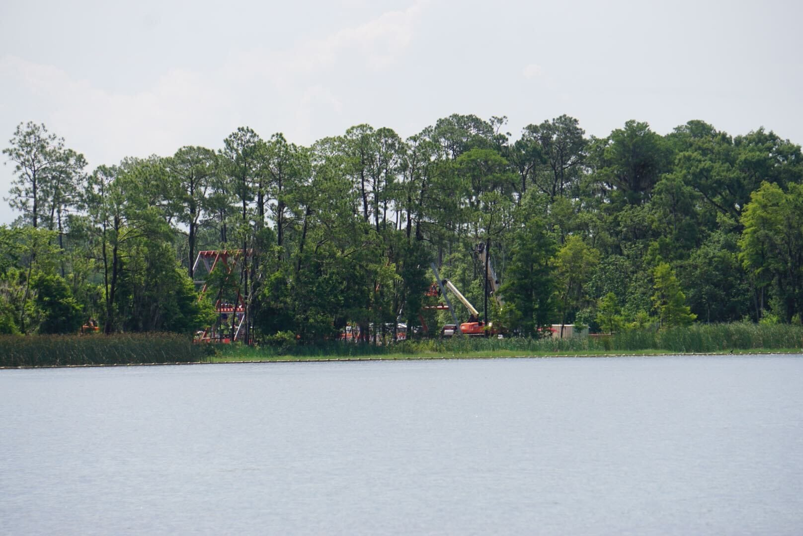 A lake with trees along the shore and colorful amusement park rides partially visible behind the trees.