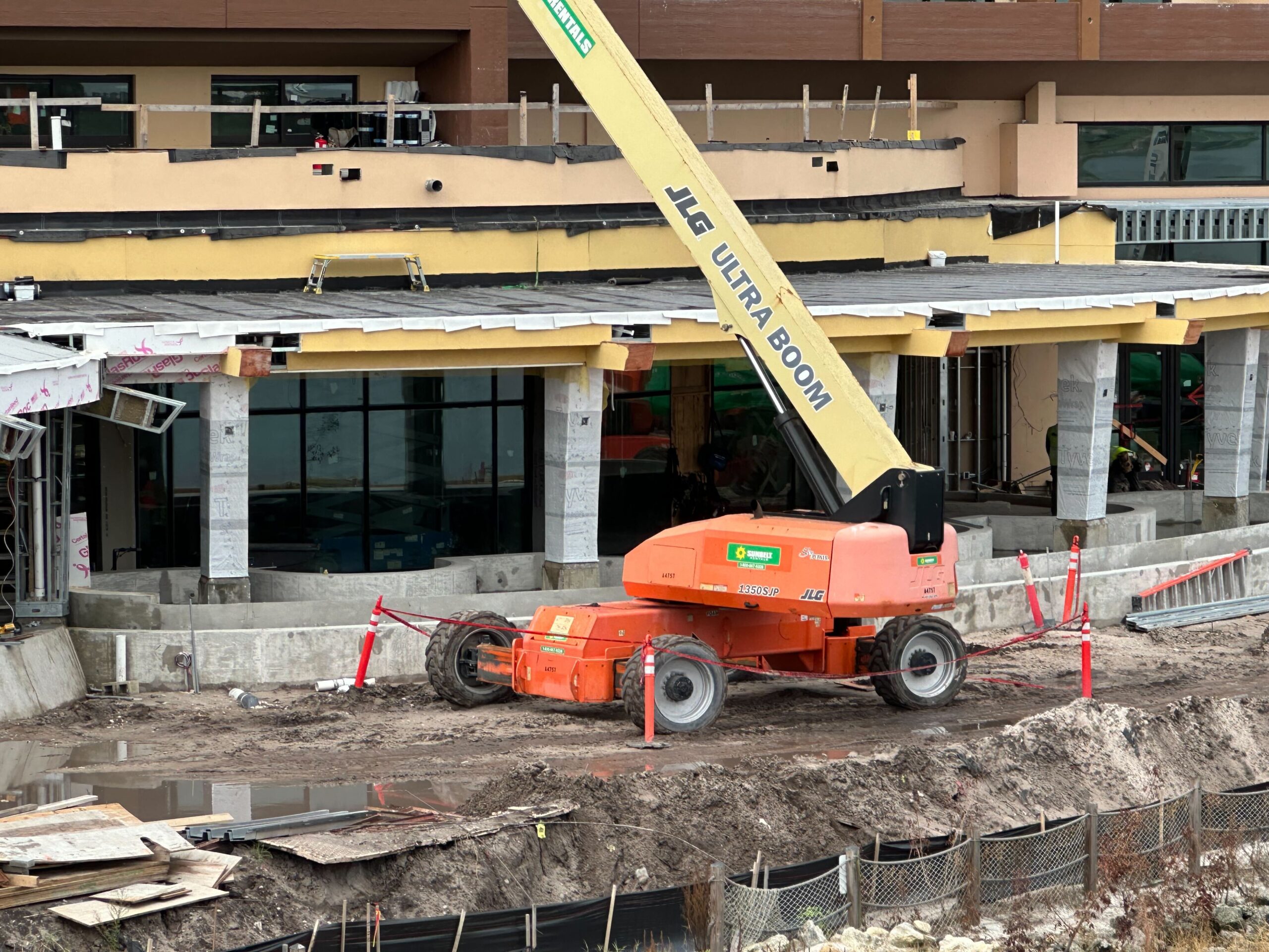 A JLG Ultra Boom lift is positioned in front of a partly constructed building, surrounded by construction materials and mud.