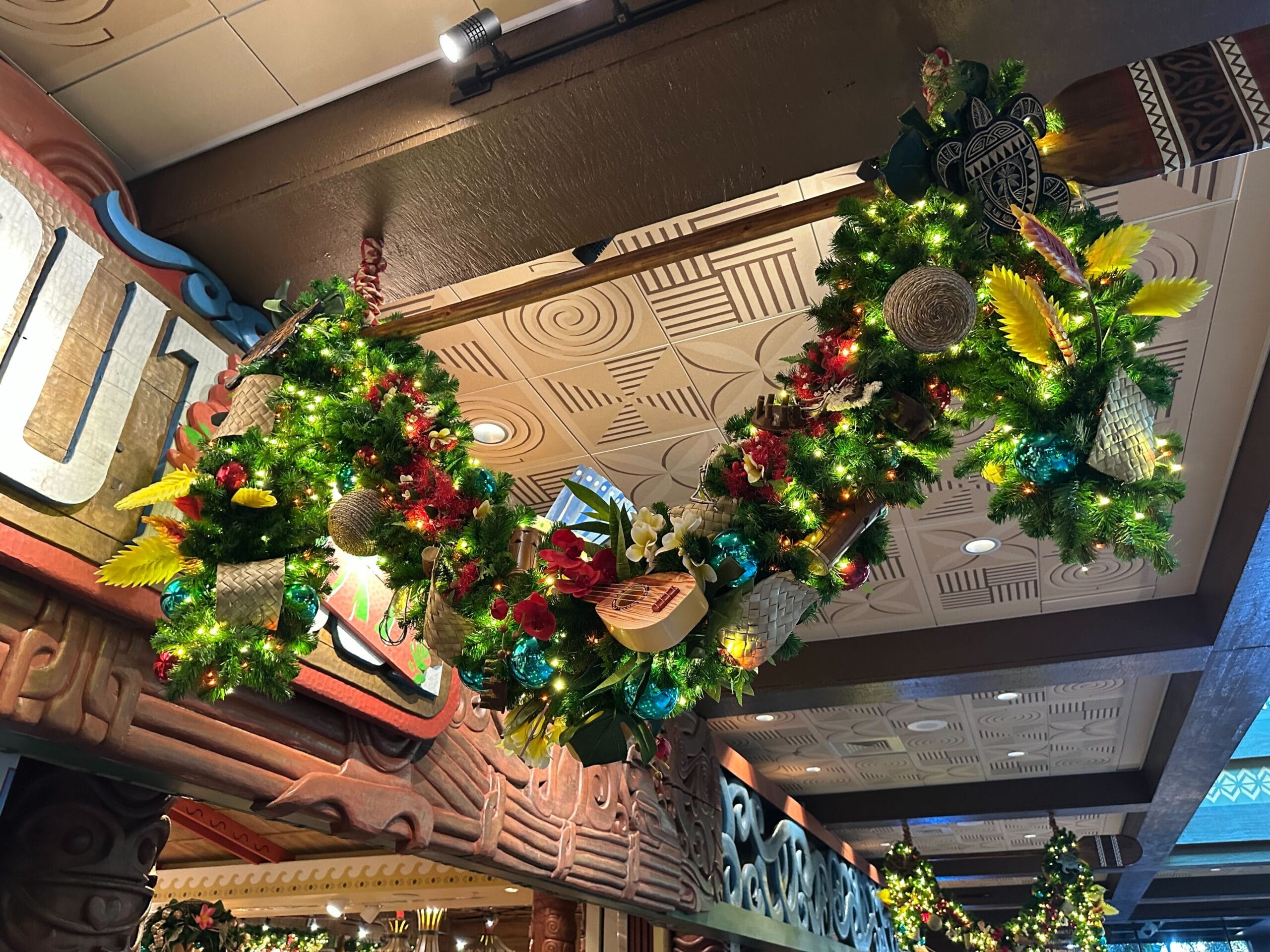 A festive garland with lights, flowers, sunflowers, and decorative ornaments is hanging from a ceiling with intricate woodwork and patterned tiles.